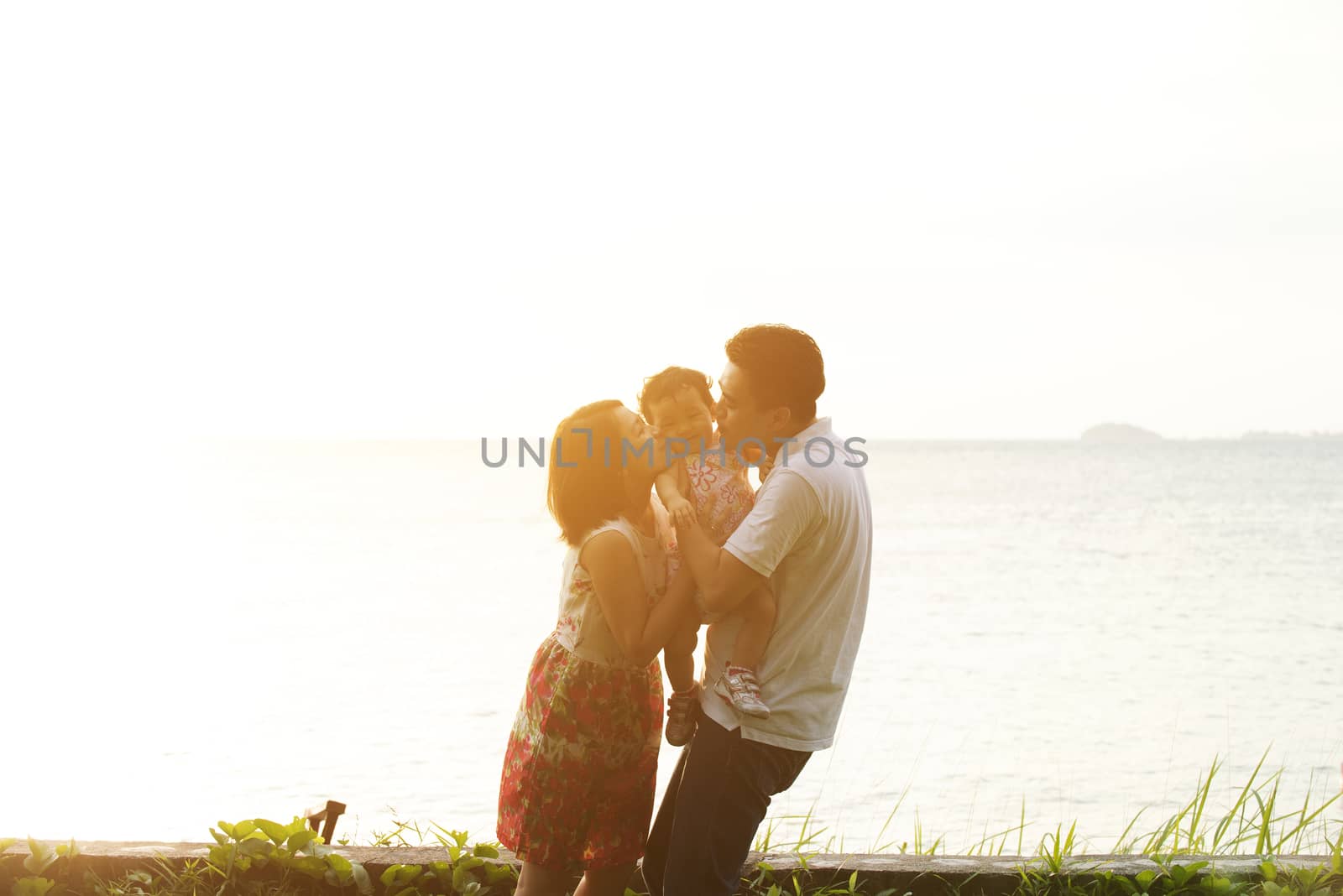 Happy family enjoying outdoor activity together, standing on coastline in beautiful sunset during holiday vacations.