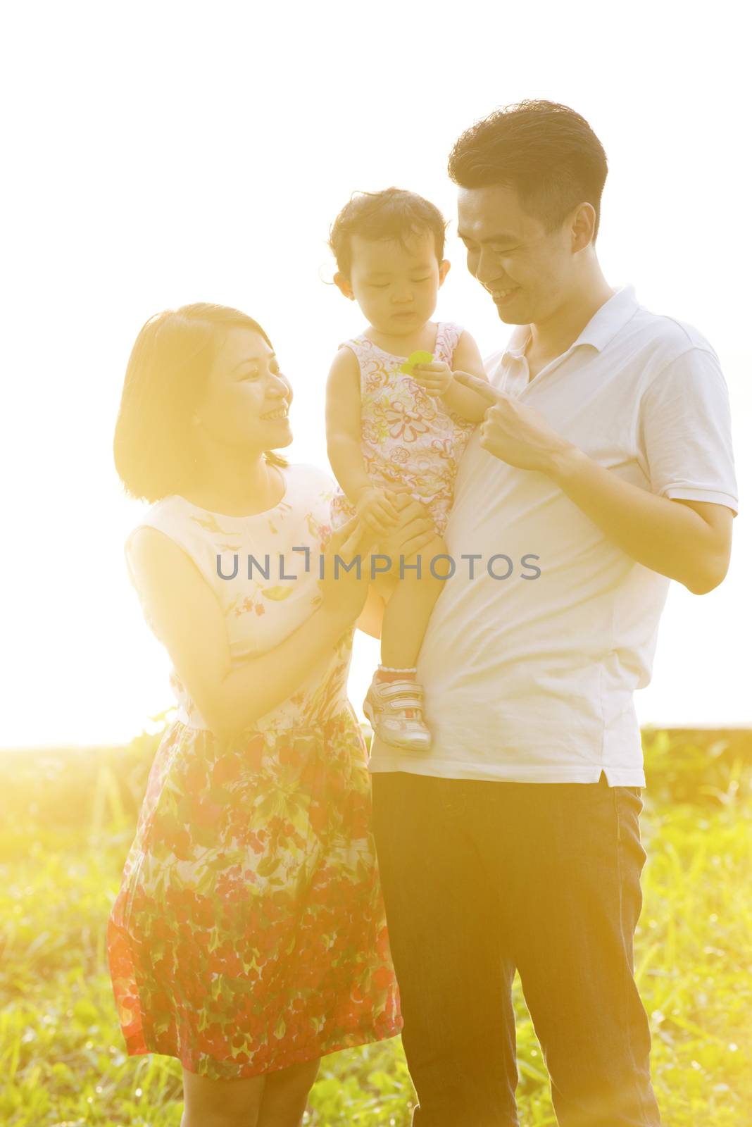 Happy Asian family enjoying outdoor activity together, standing on garden park lawn in beautiful sunset during holiday vacations.