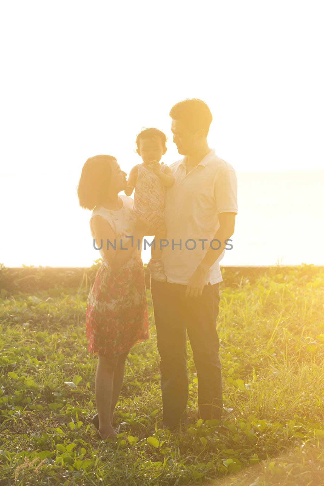 Happy Asian family enjoying outdoor activity together, standing on garden park in beautiful sunset during holiday vacations.