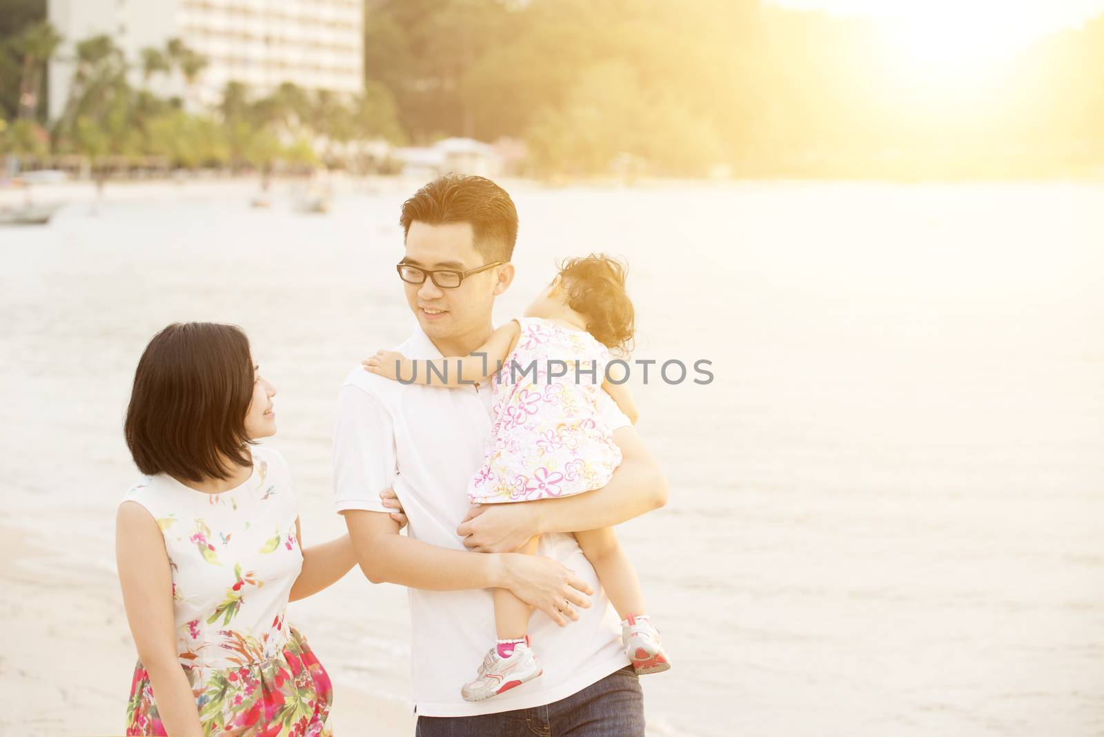 Portrait of happy family enjoying outdoor activity together, walking on coastline in beautiful sunset during holiday vacations.
