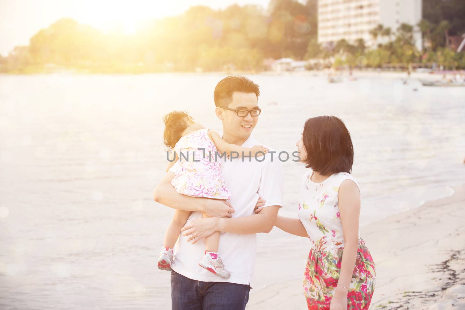 Portrait of Asian family enjoying outdoor activity together, walking on coastline in beautiful sunset during holiday vacations.