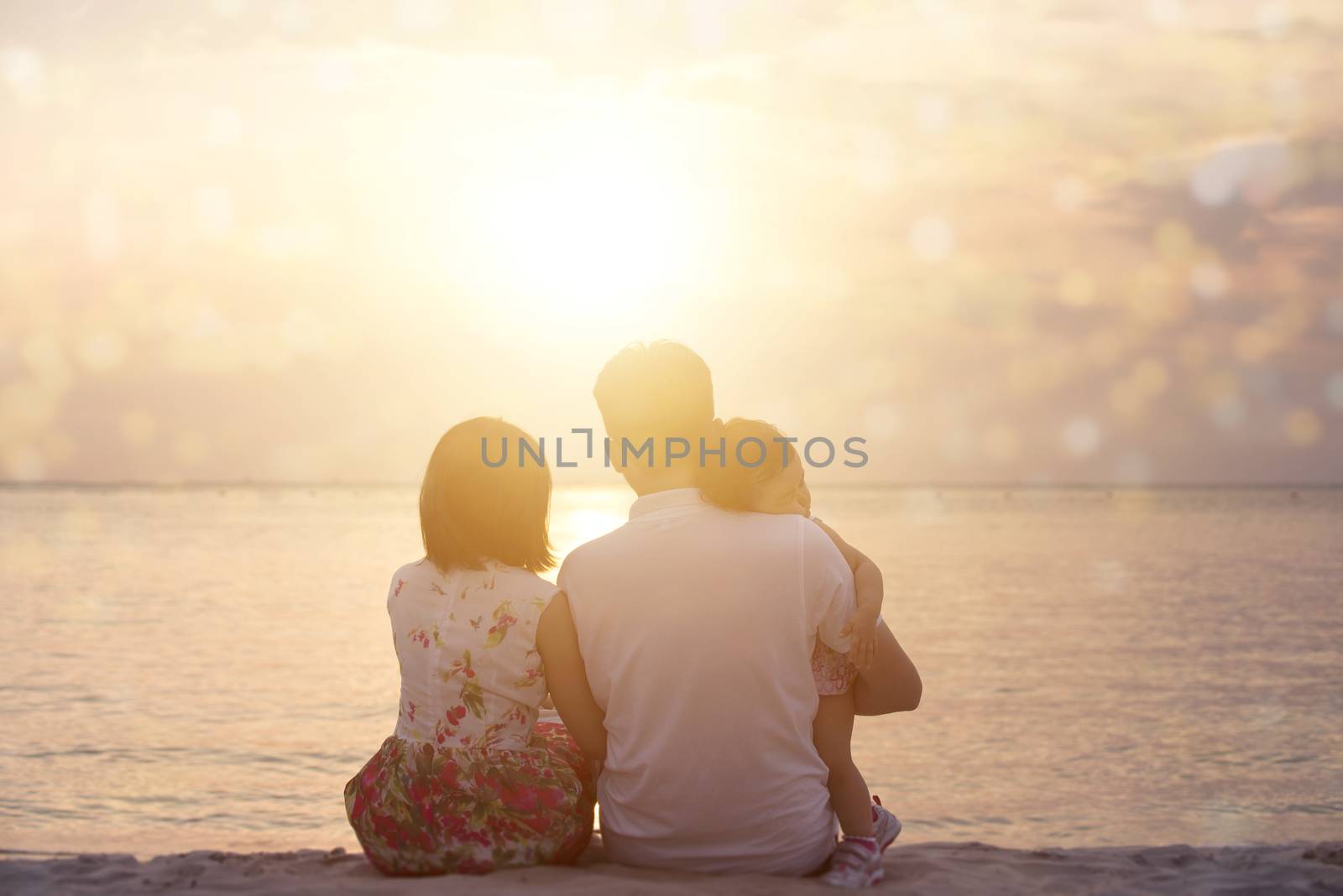 Rear view of family enjoying outdoor activity together, sitting on coastline in beautiful sunset during holiday vacations.