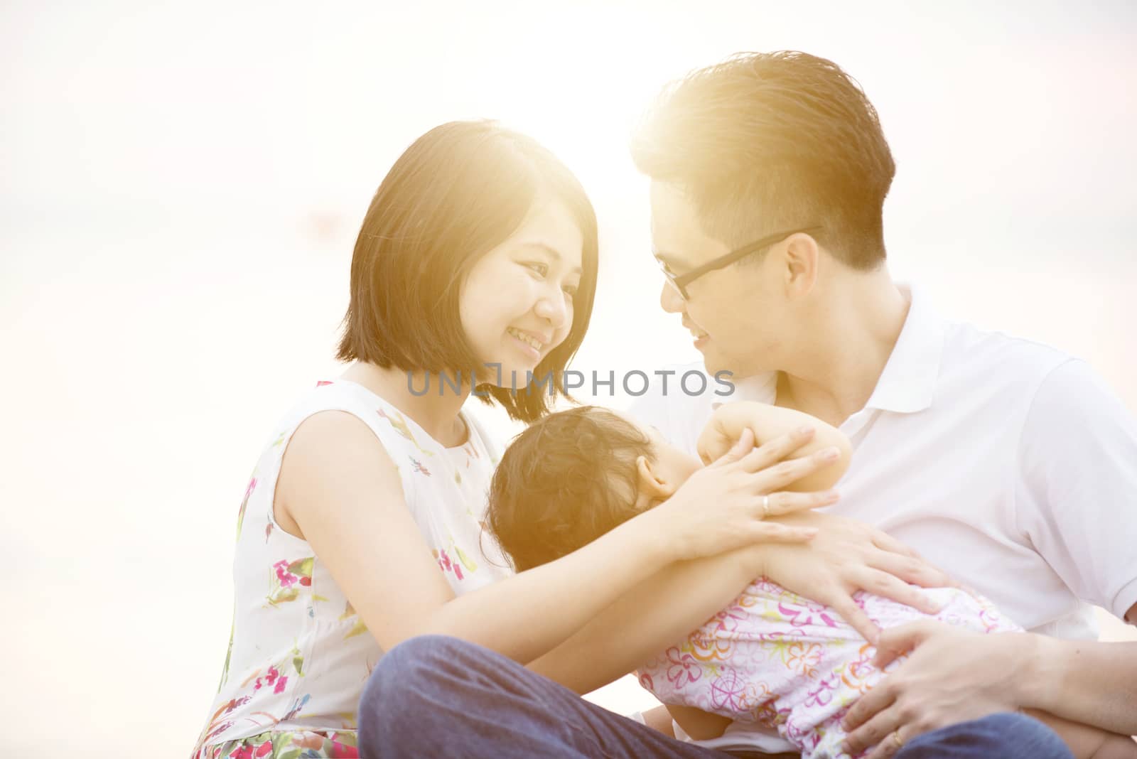 Young Asian family outdoor portrait, having fun time together on beach in sunset during vacations.