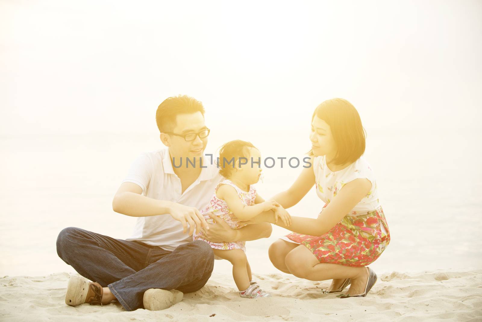 Happy Asian family outdoor activity, playing together on beach in sunset during vacations.