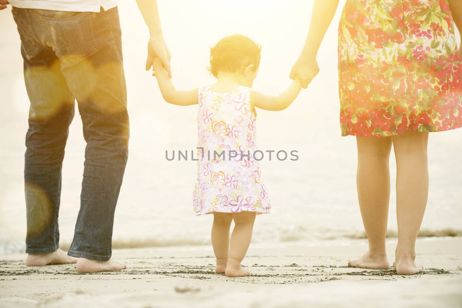 Happy Asian family outdoor activity, holding hands together walking on sand seaside in sunset during vacations.