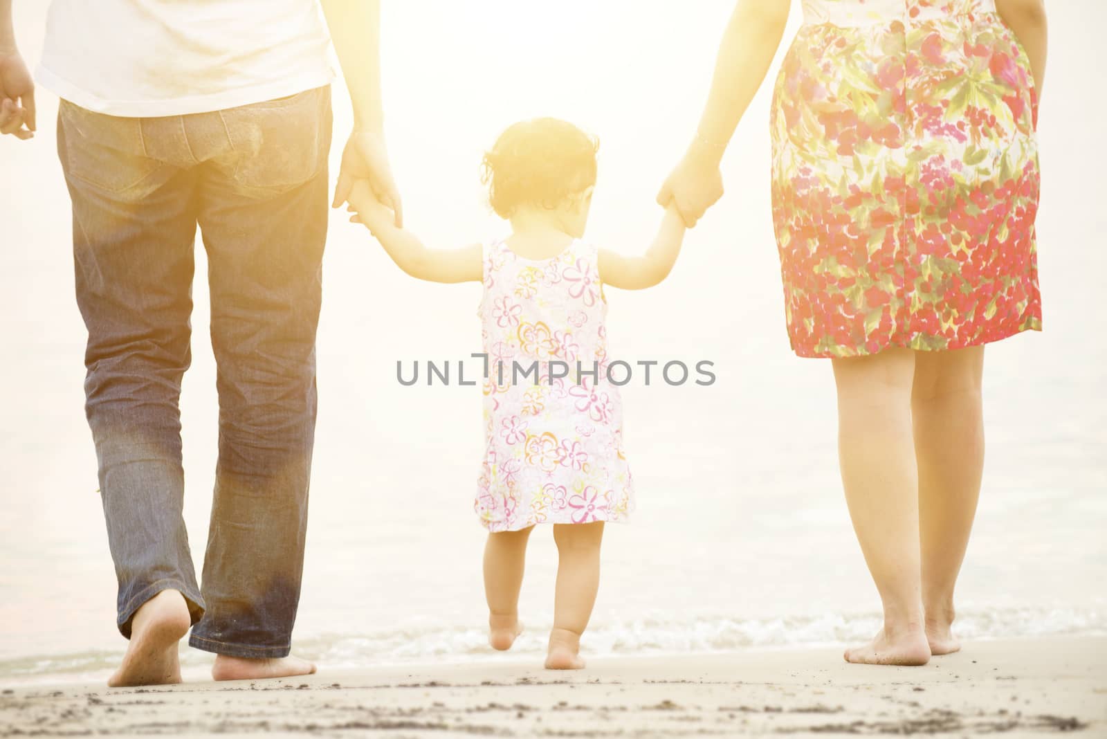 Happy Asian family outdoor activity, holding hands together walking on sandy beach in sunset during vacations.