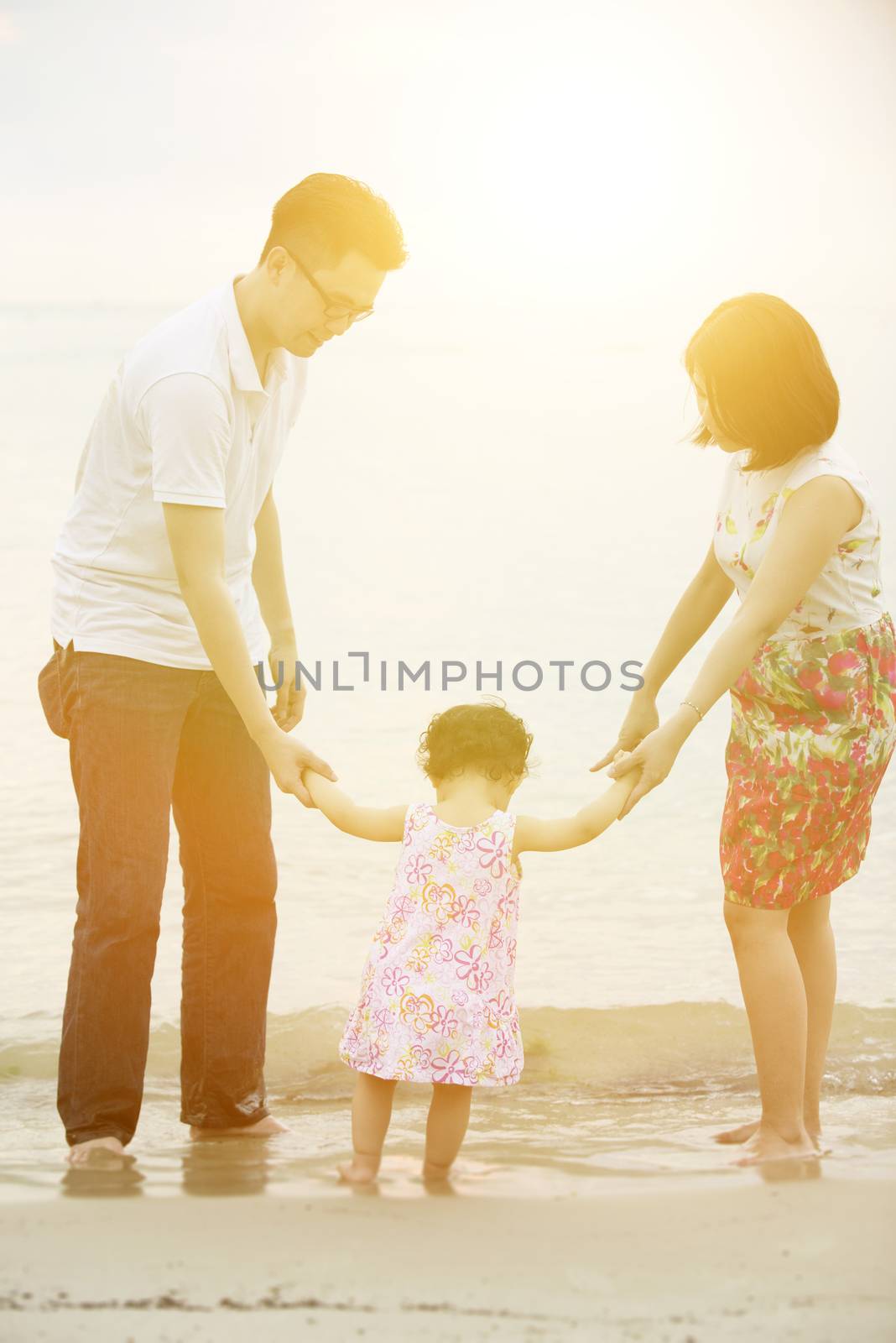 Happy Asian family outdoor activity, holding hands together walking at beach in sunset during vacations.