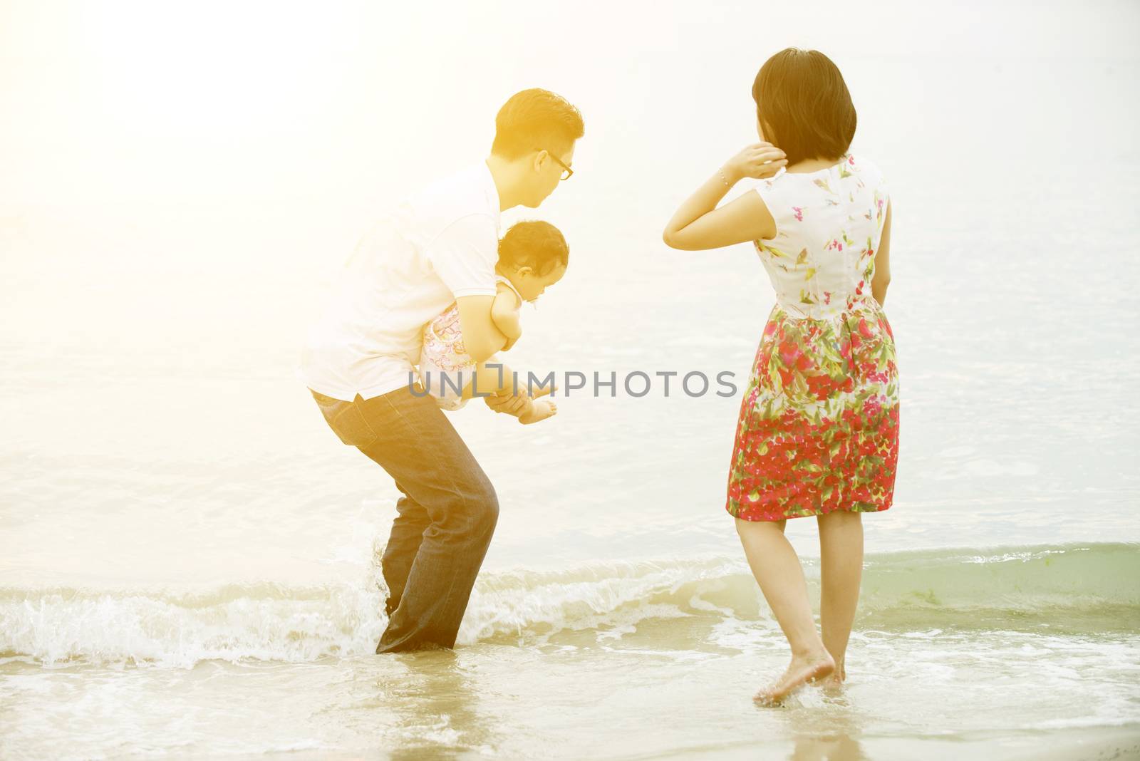 Happy Asian family outdoor activity, playing water together at beach in sunset during vacations.