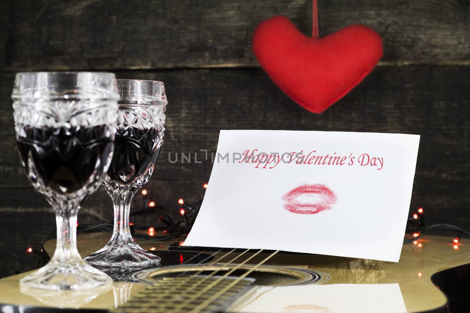 Happy Valentine's Day Kiss On White Paper Resting on Acoustic Guitar With Vine Glasses, Lights and Heart