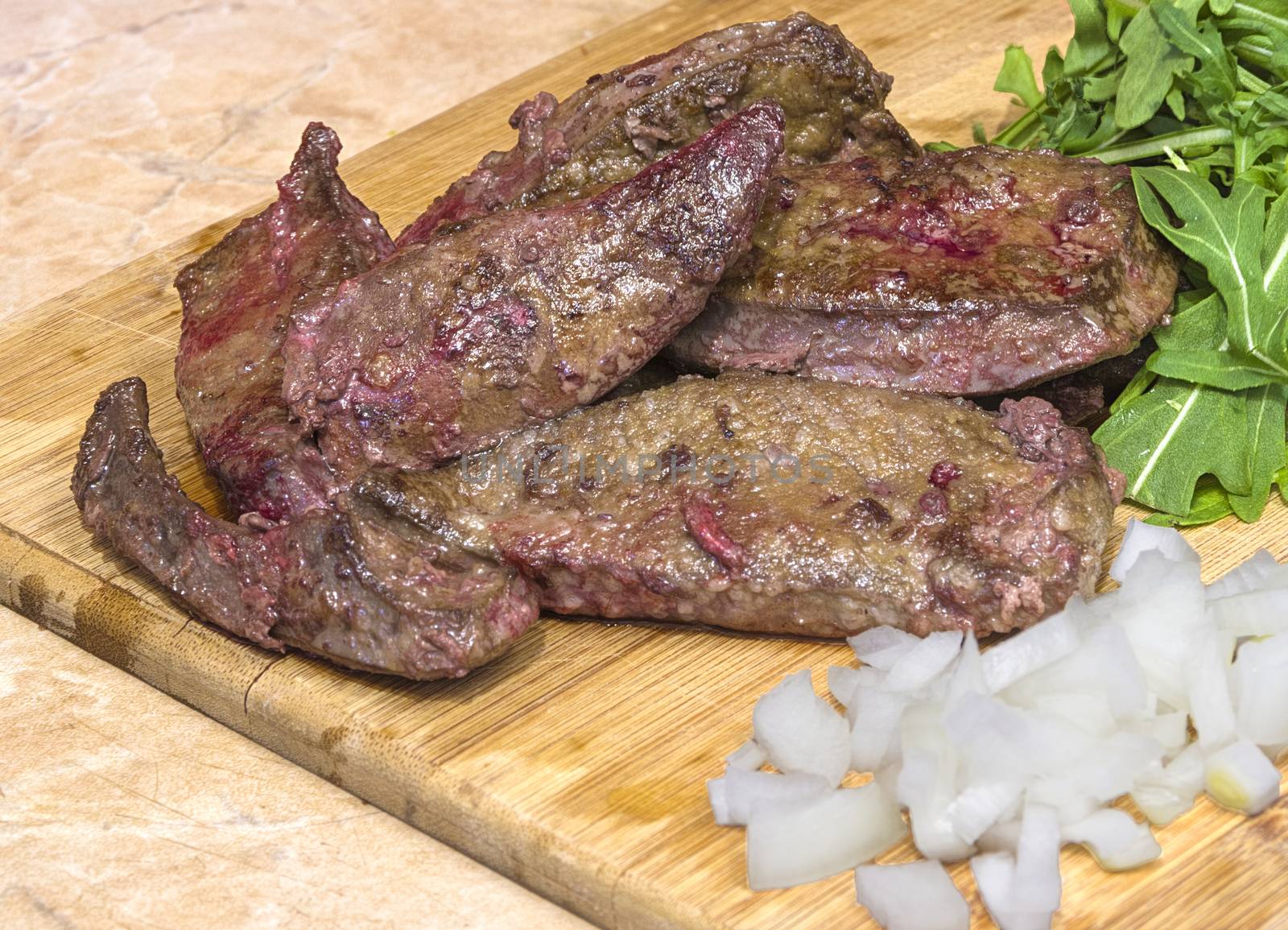 grilled beef liver with onions and herbs on a wooden cutting board