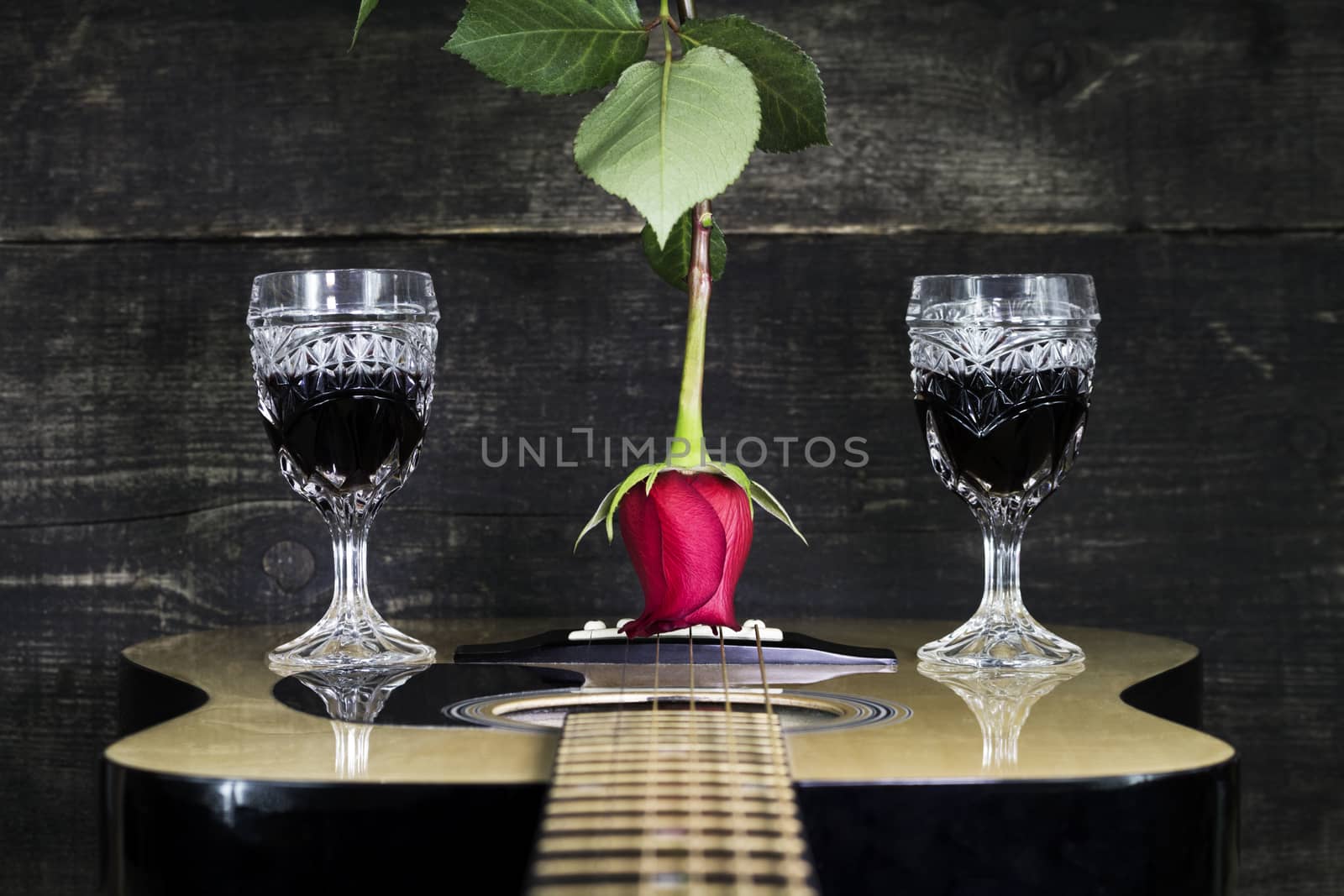 Red Rose and Wine Glasses Resting On Acoustic Guitar With Wooden by alexandarilich