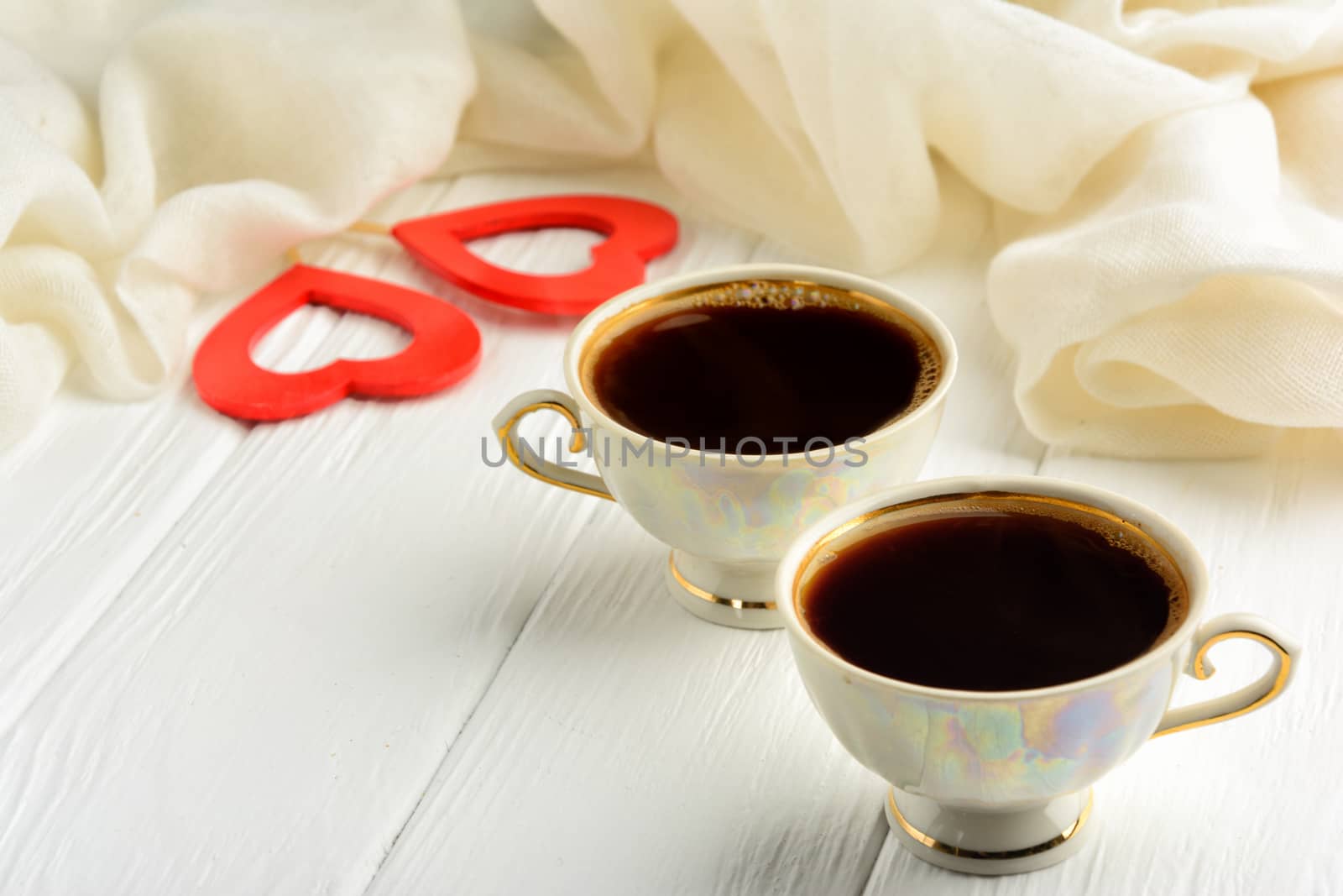 Two cups of morning fragrant coffee on St. Valentine's Day against the background of two red hearts and a white scarf