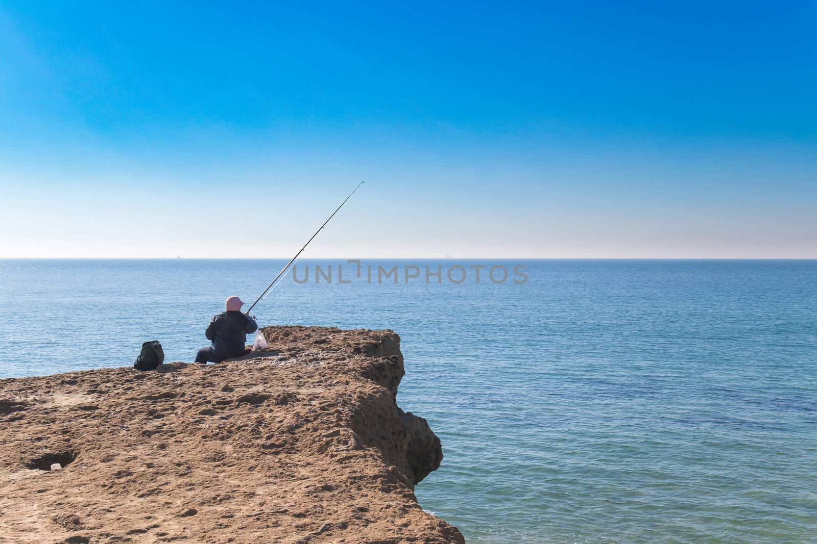 old person fishing in the edge of the ocean on top of sedemenary rock