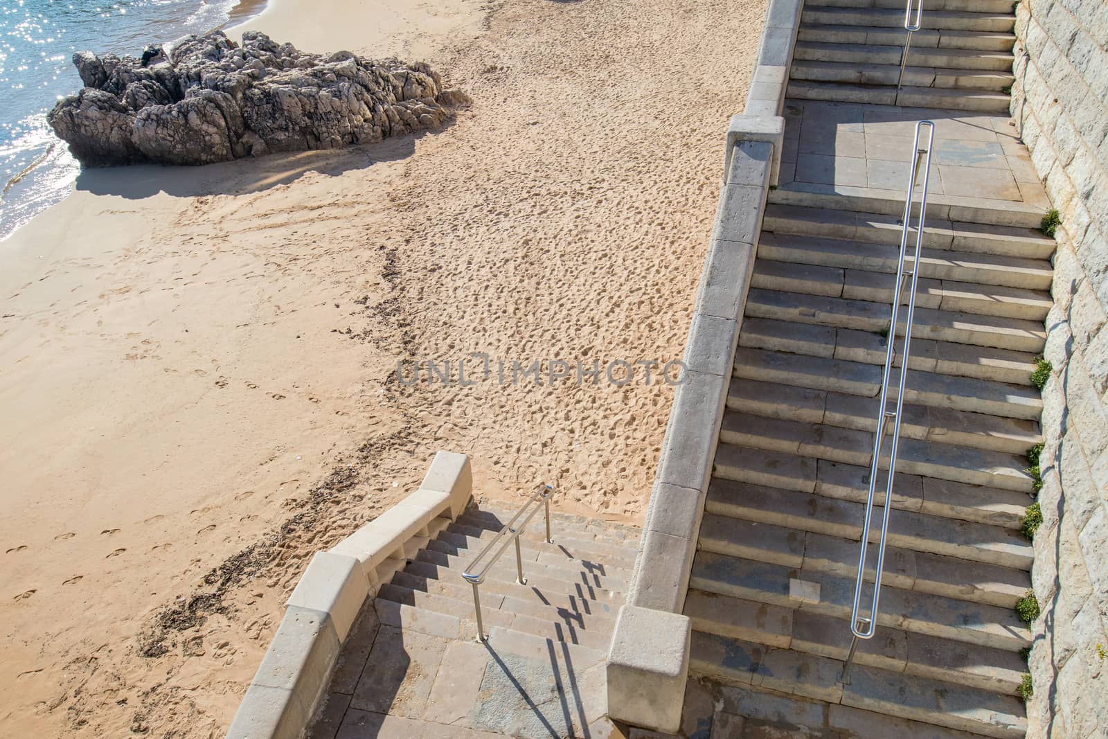two flights of stairs to access a fine sand beach with a rock just at the edge of the water