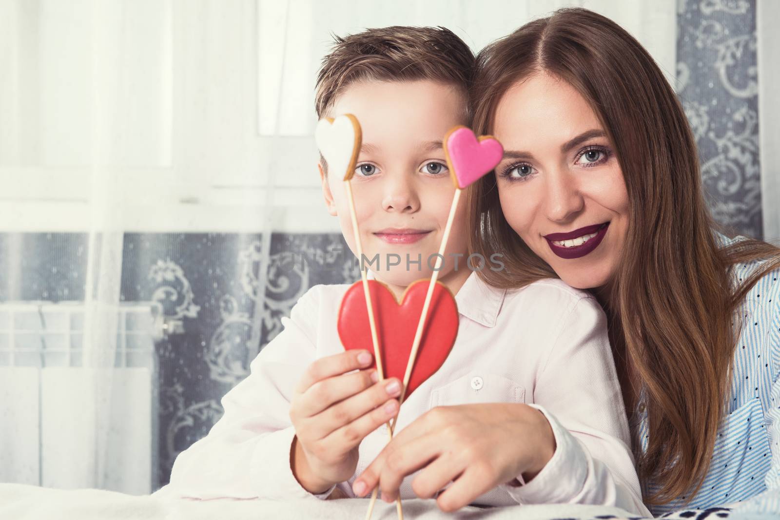 Happy Valentines Day or Mother day. Young boy spend time with his mum and celebrate with gingerbread heart cookies on a stick.