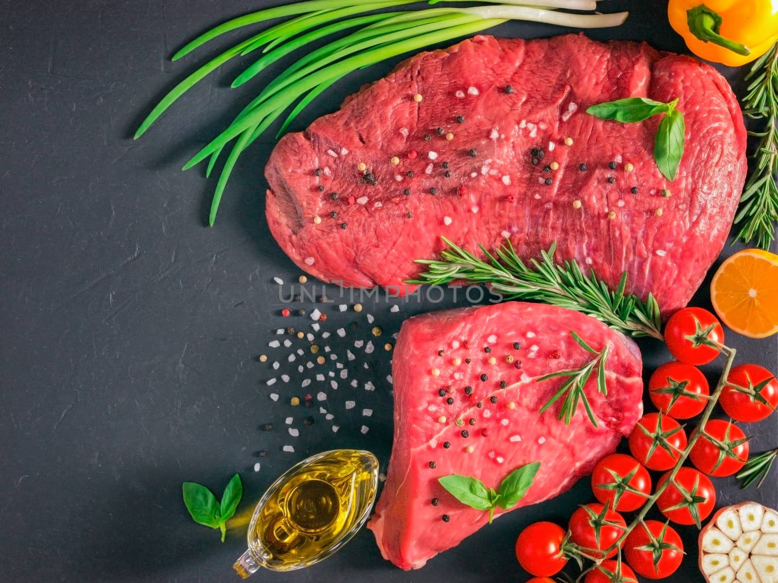 Raw meat. Raw beef steak on dark board with fresh herbs, vegetables, seasonings and spices. Top view or flat lay. Copy space