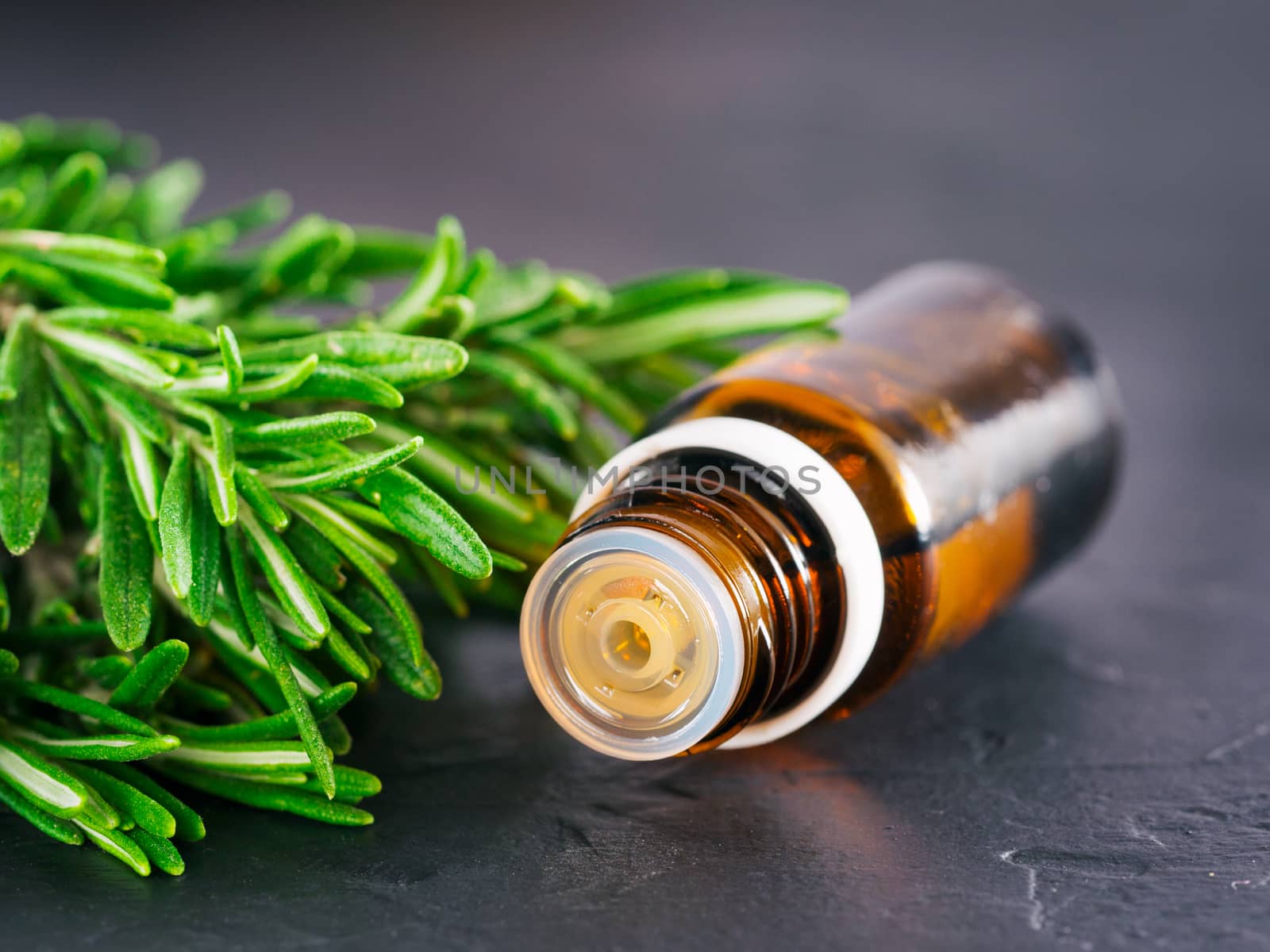 Rosemary essential oil in dark glass bottle and fresh rosemary on dark background with copy space