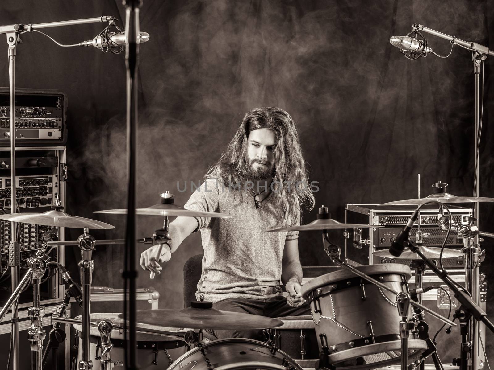 Photo of a young male drummer with long hair playing his drum set.

