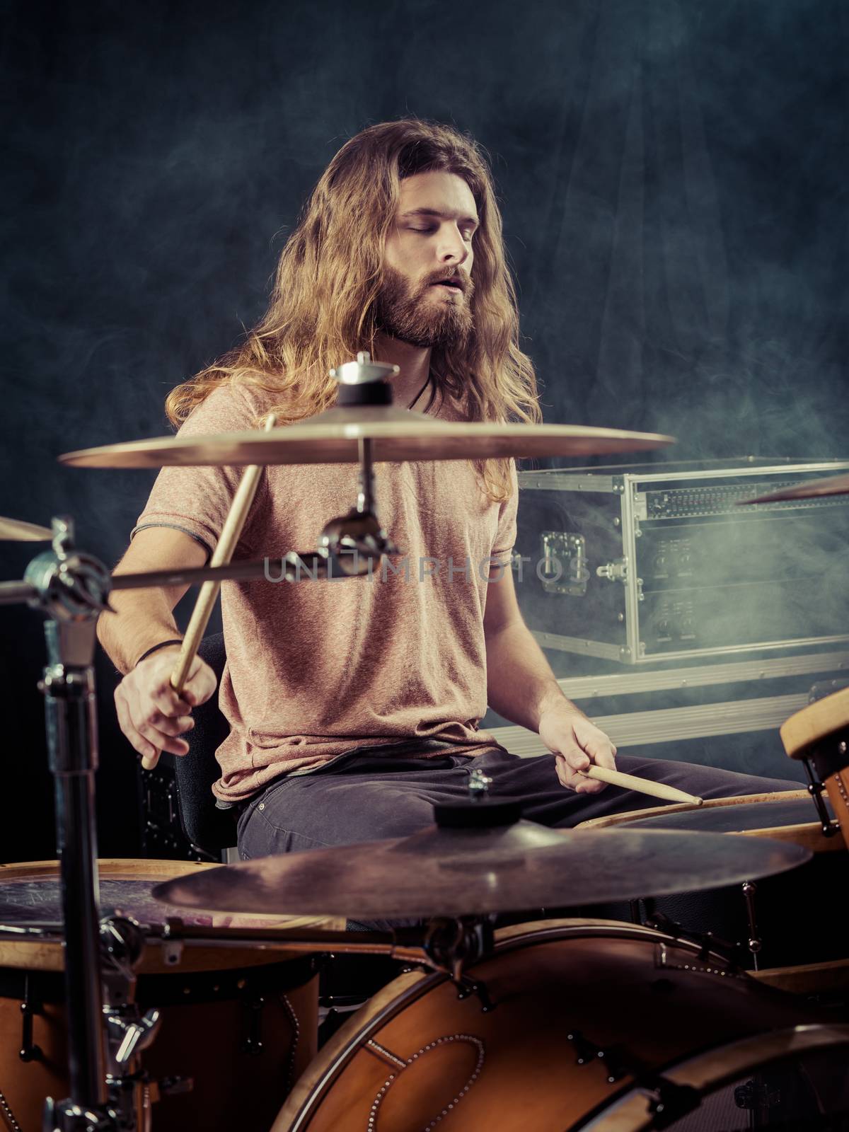 Photo of a young male drummer with long hair playing his drum set. Filtered for vintage look.

