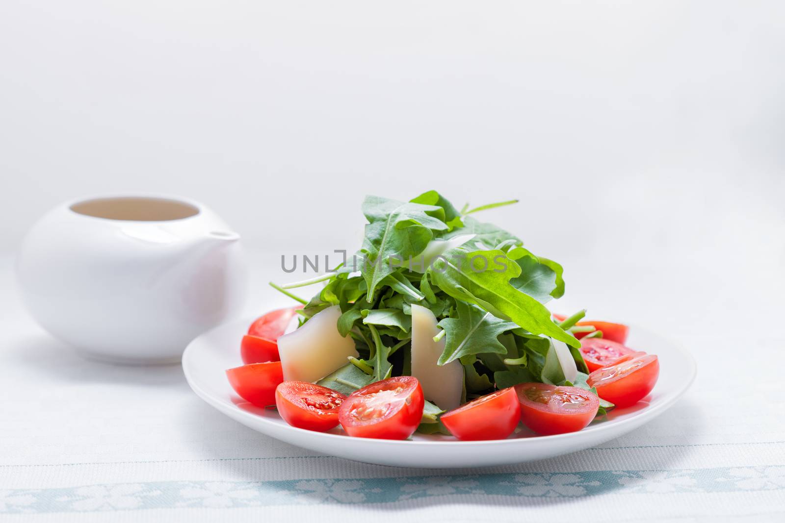 Salad with arugula, tomatoes served on a white plate
