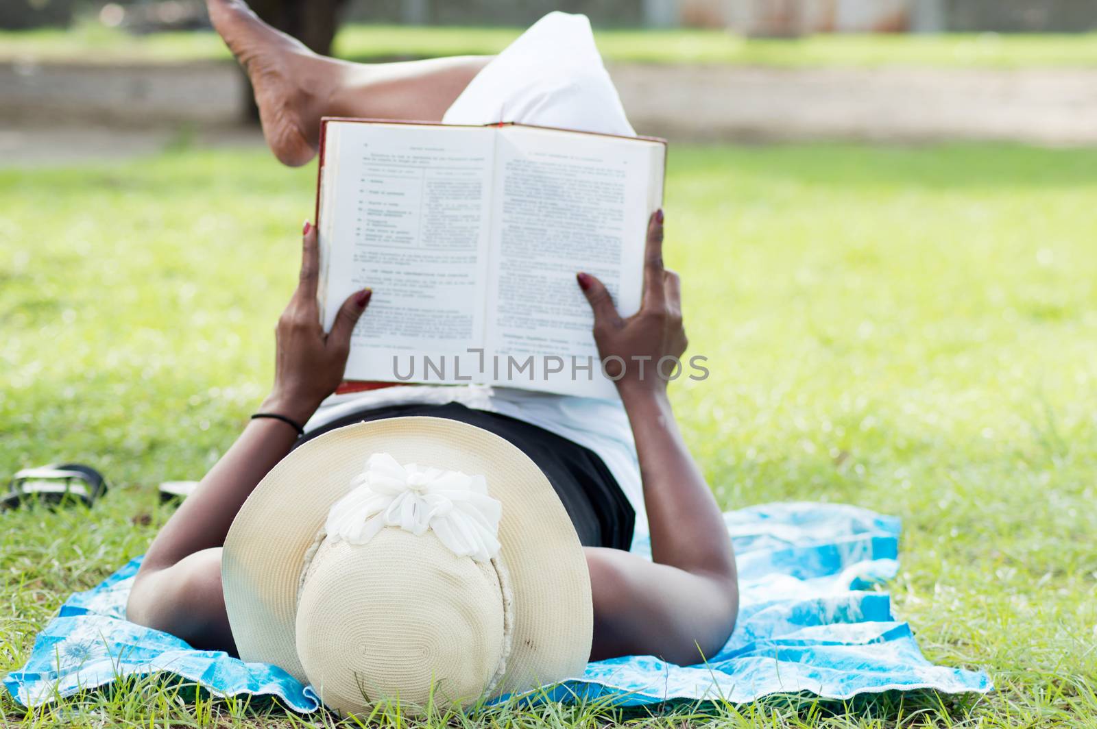 This young woman lying in the shade of a tree  is reading quietly.