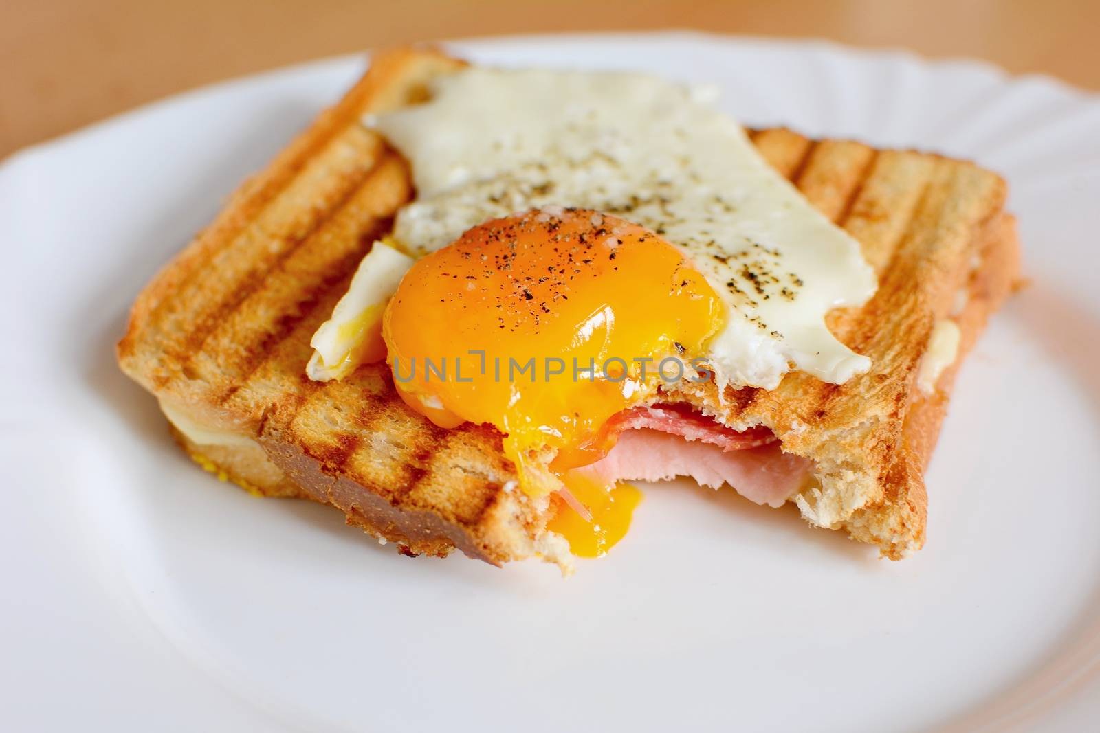 Ham and cheese toast with fried egg on top with missing bite.