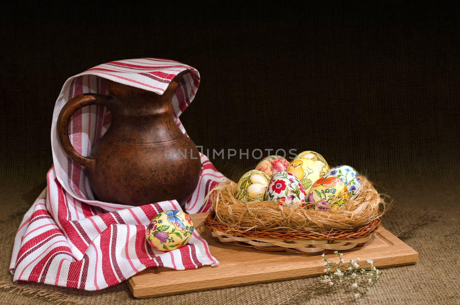 Decoupage Easter eggs in a basket and a jug under the towel, the dark background is burlap. Selective focus.