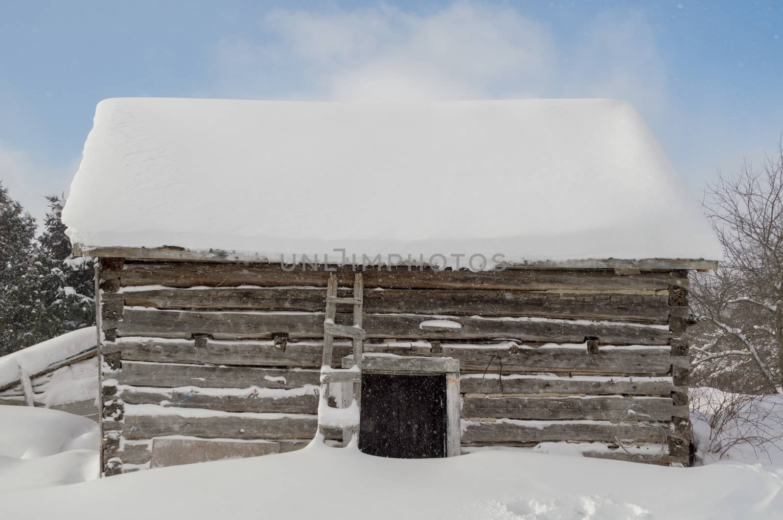 Old outbuilding sawn log cabin with it snowing and clouds and blue sky