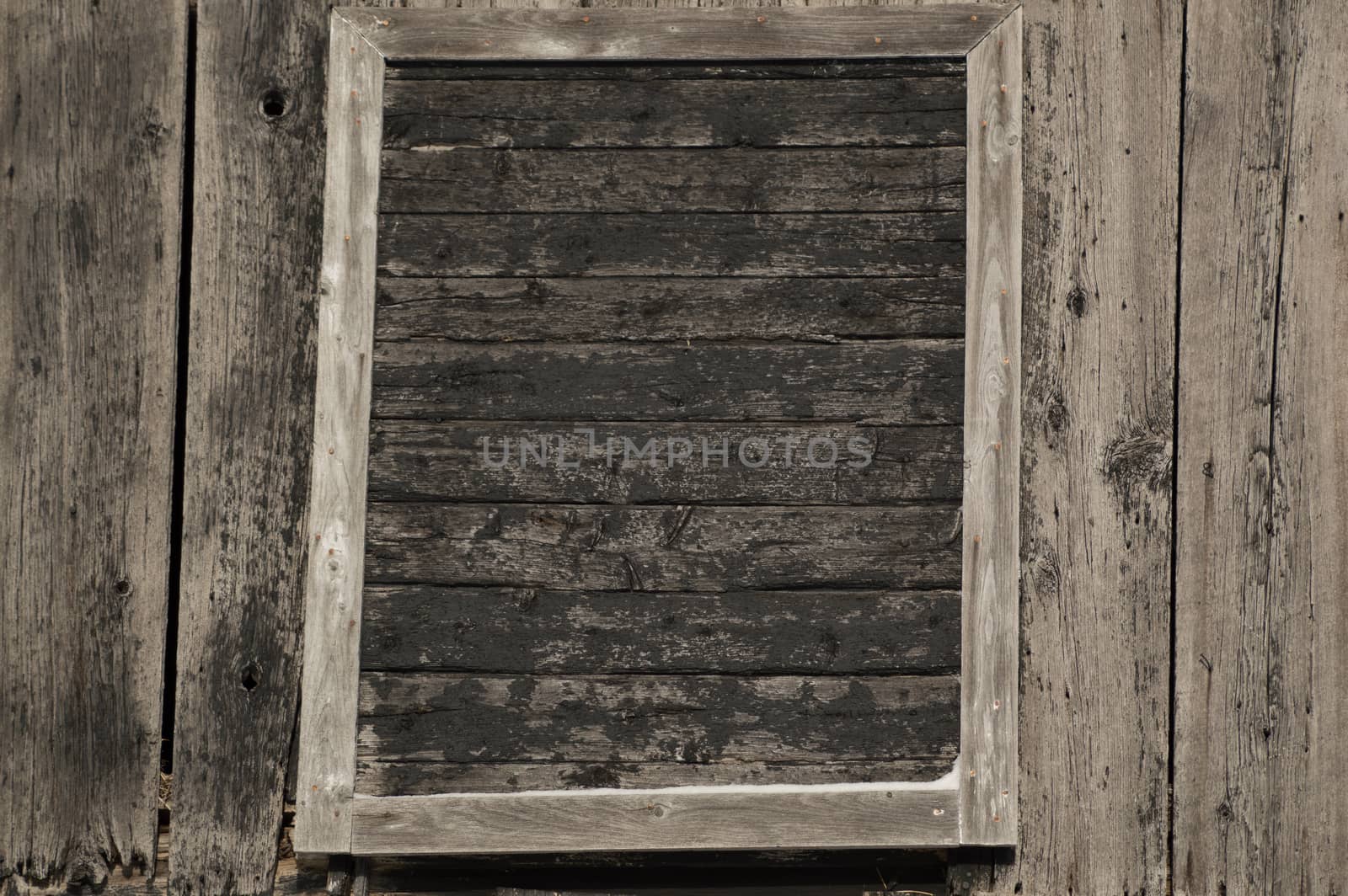 This old farm building has weathered grey and black painted barn board. An old door or window is framed on the side and peeling cracked black paint.