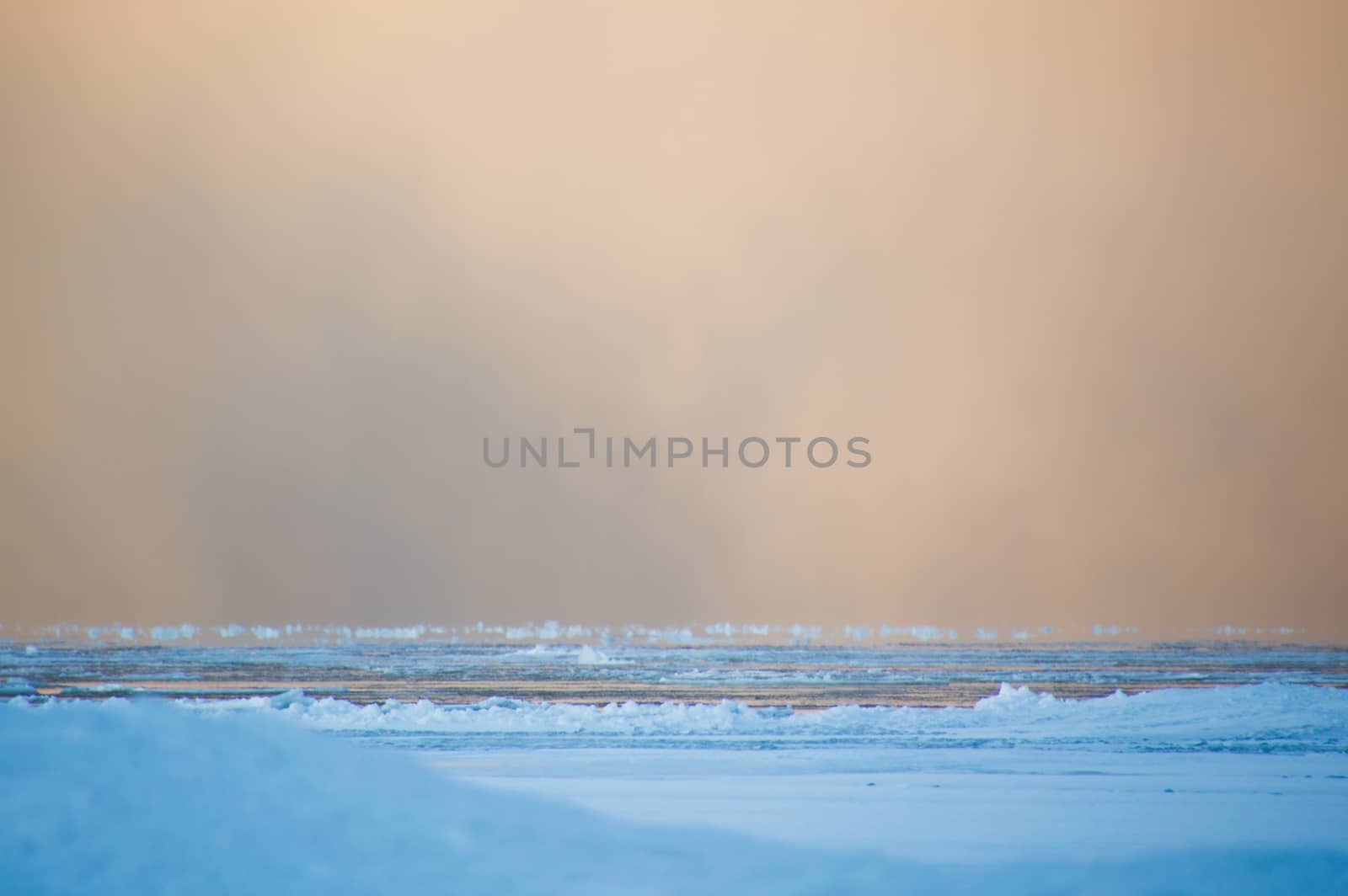 Sidelit snow squall clouds rolling in across the frozen Lake Huron at sunrise.  Ice floats on the still calm water.