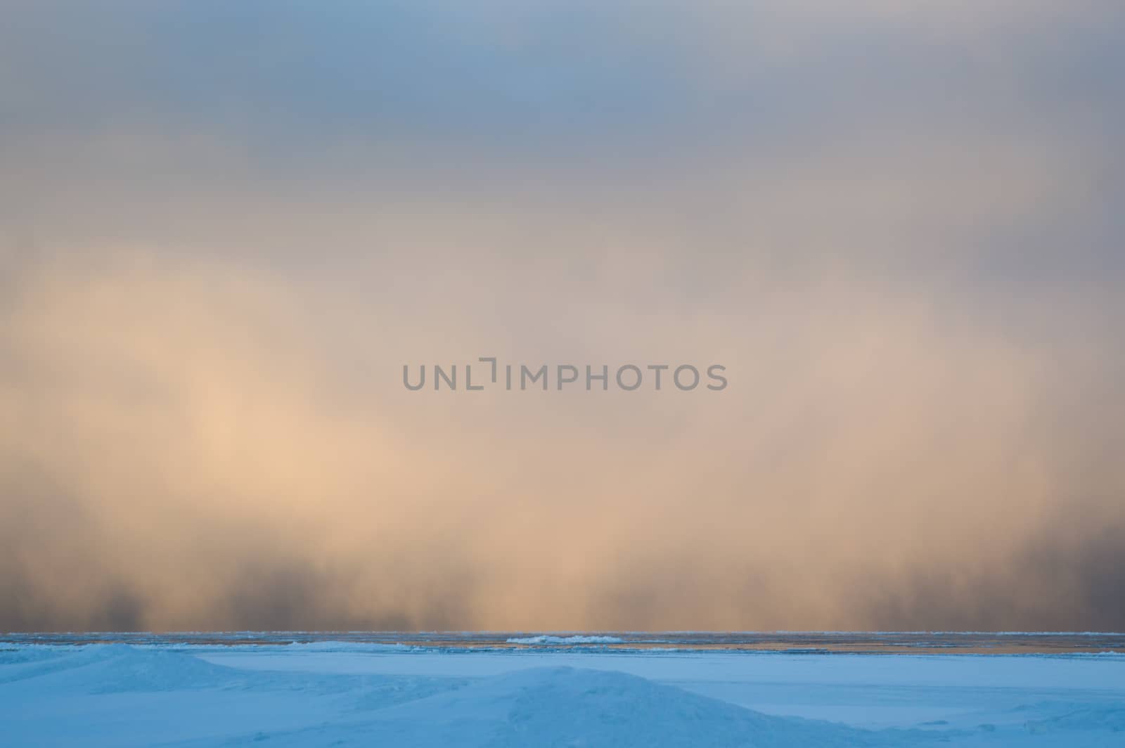 Sidelit snow squall clouds rolling in across the frozen Lake Huron at sunrise.  Ice floats on the still calm water.