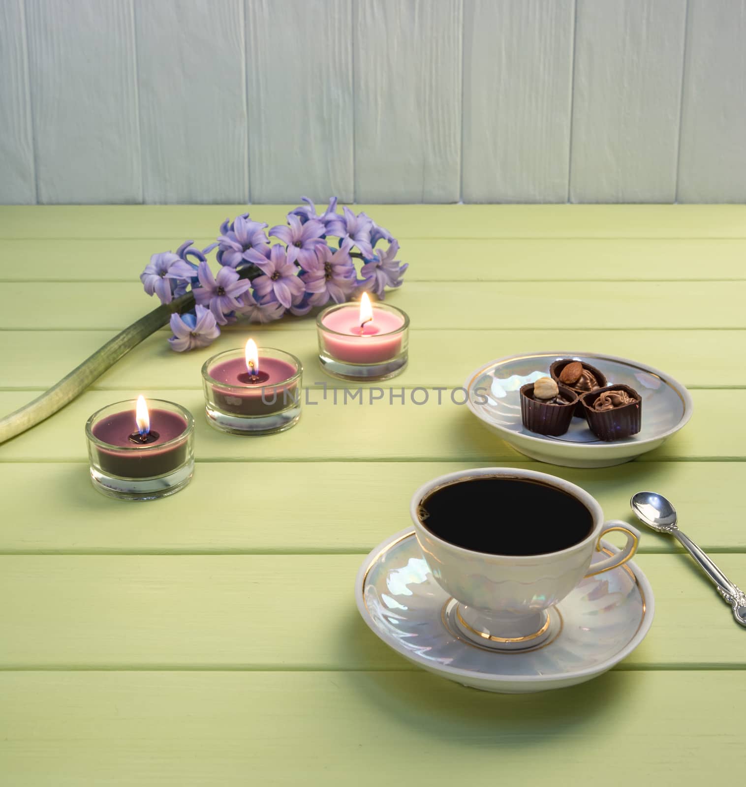 Cup of black coffee, candles and flowers on a wooden background.