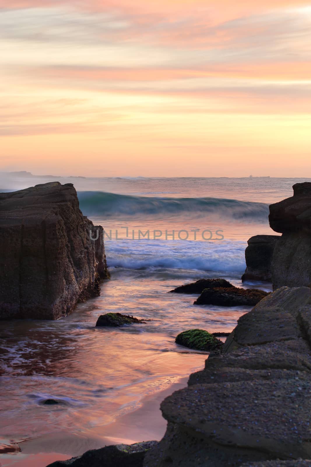 Beautiful colours in the wispy wind swept sky and tidal waves wash in between rocks on the beach