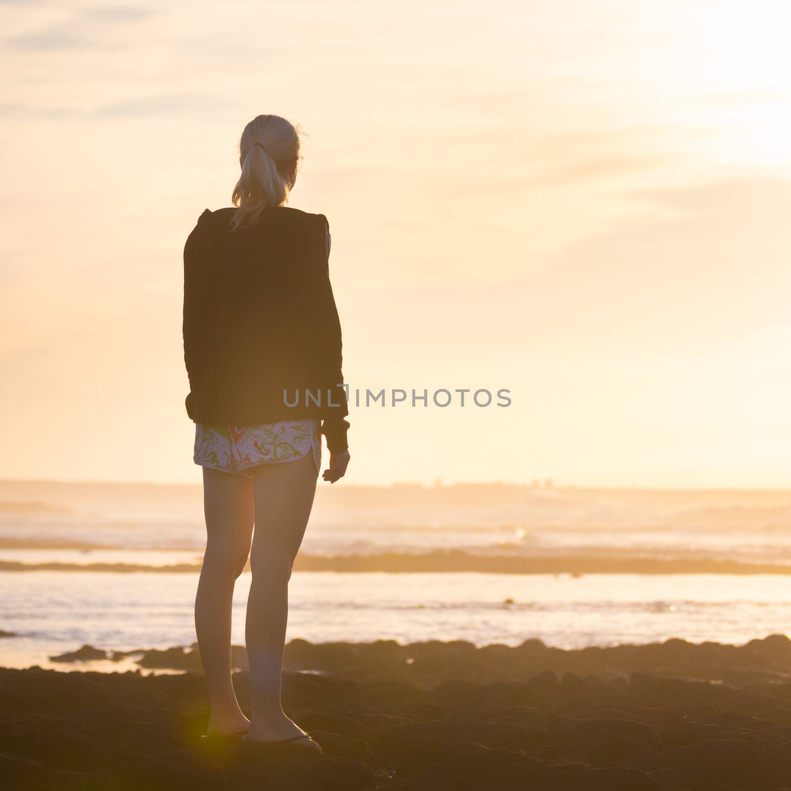 Silhouette of casualy dressed sporty woman watching sunset at the beach.