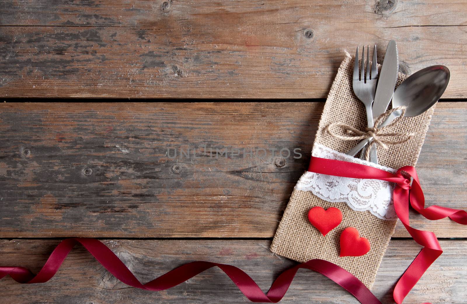 Valentines day cutlery set inside pouch with red hearts and silk ribbon over a wooden background