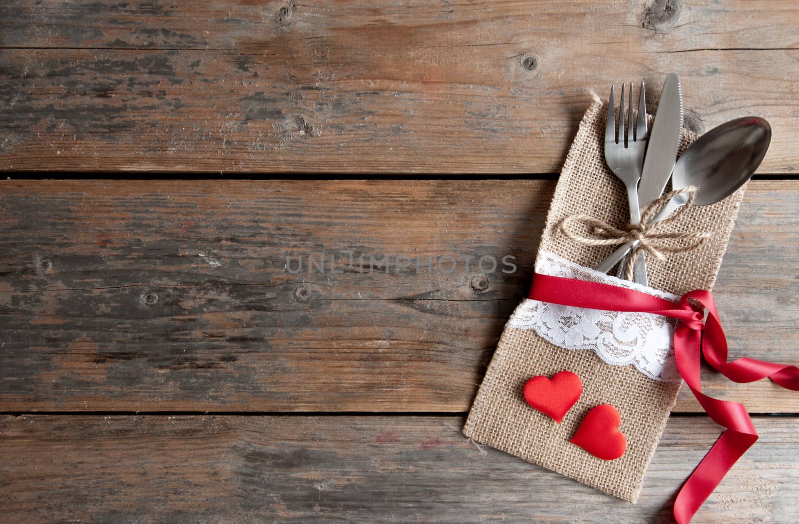 Cutlery set inside pouch with two red hearts and silk ribbon over a wooden background