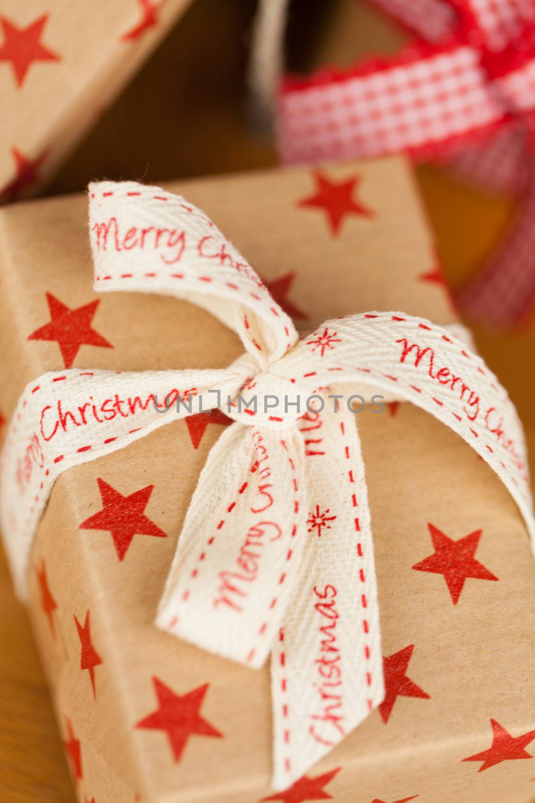 Close up vertical shot of several present boxes in kraft paper decorated with ribbons and red star pattern, on wooden surface