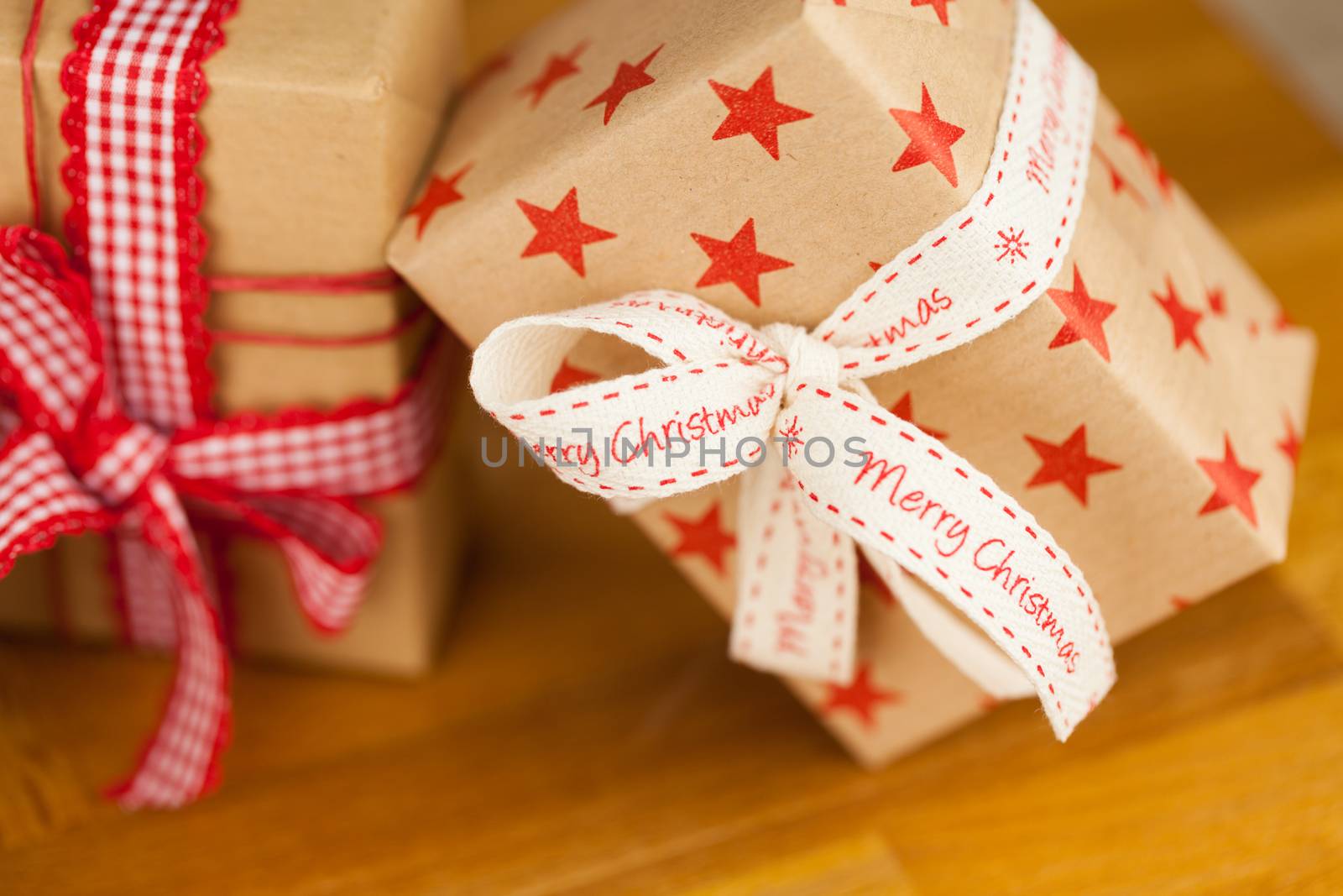 Close up vertical shot of several present boxes in kraft paper decorated with ribbons and red star pattern, on wooden surface