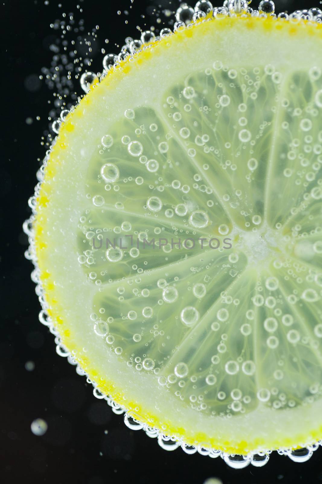 Close-up view of lemon slice under carbonated water with bubbles, refresher concept on black background