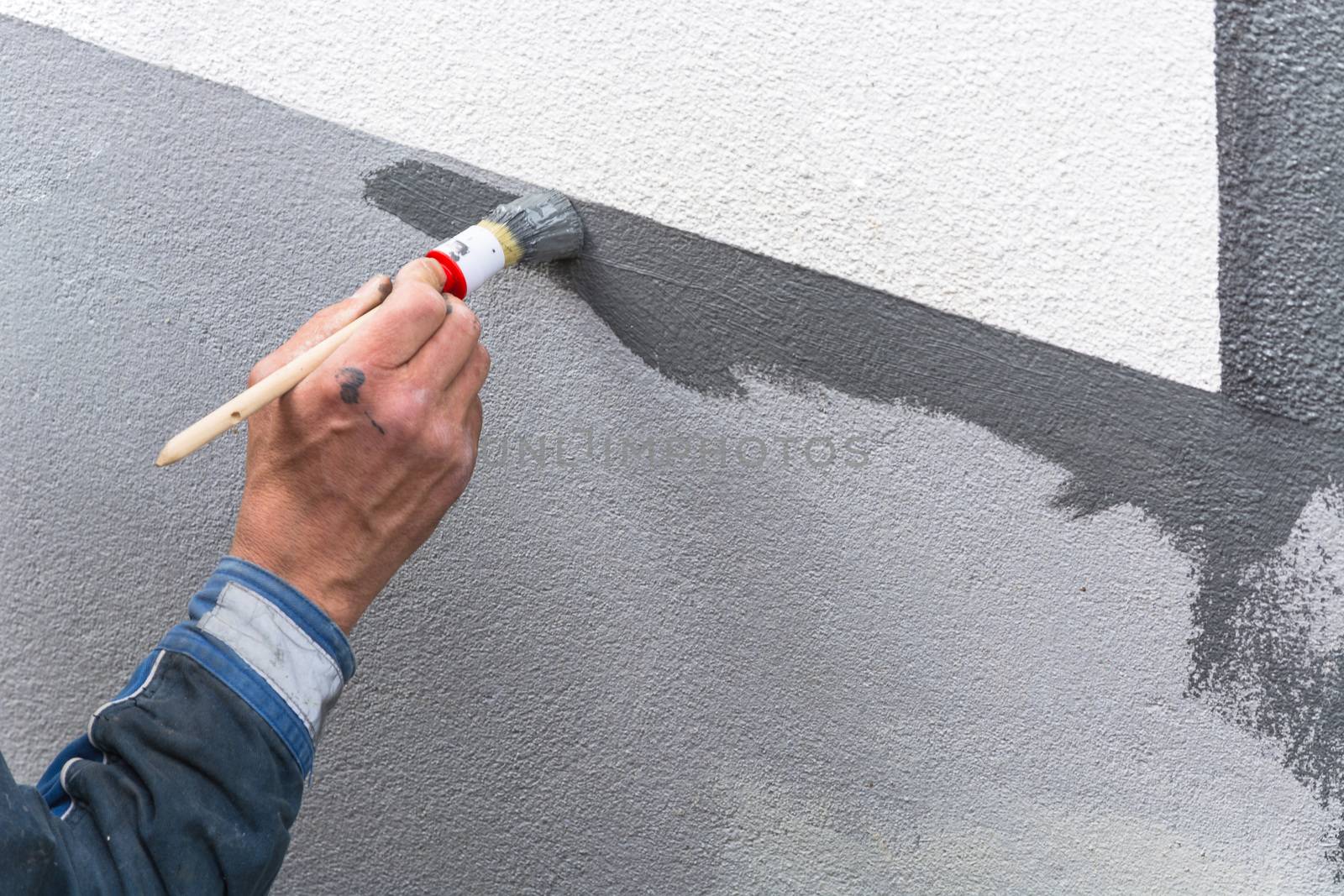 Close-up, arm of a house painter with paint roller in hand painting a house wall with gray paint.

