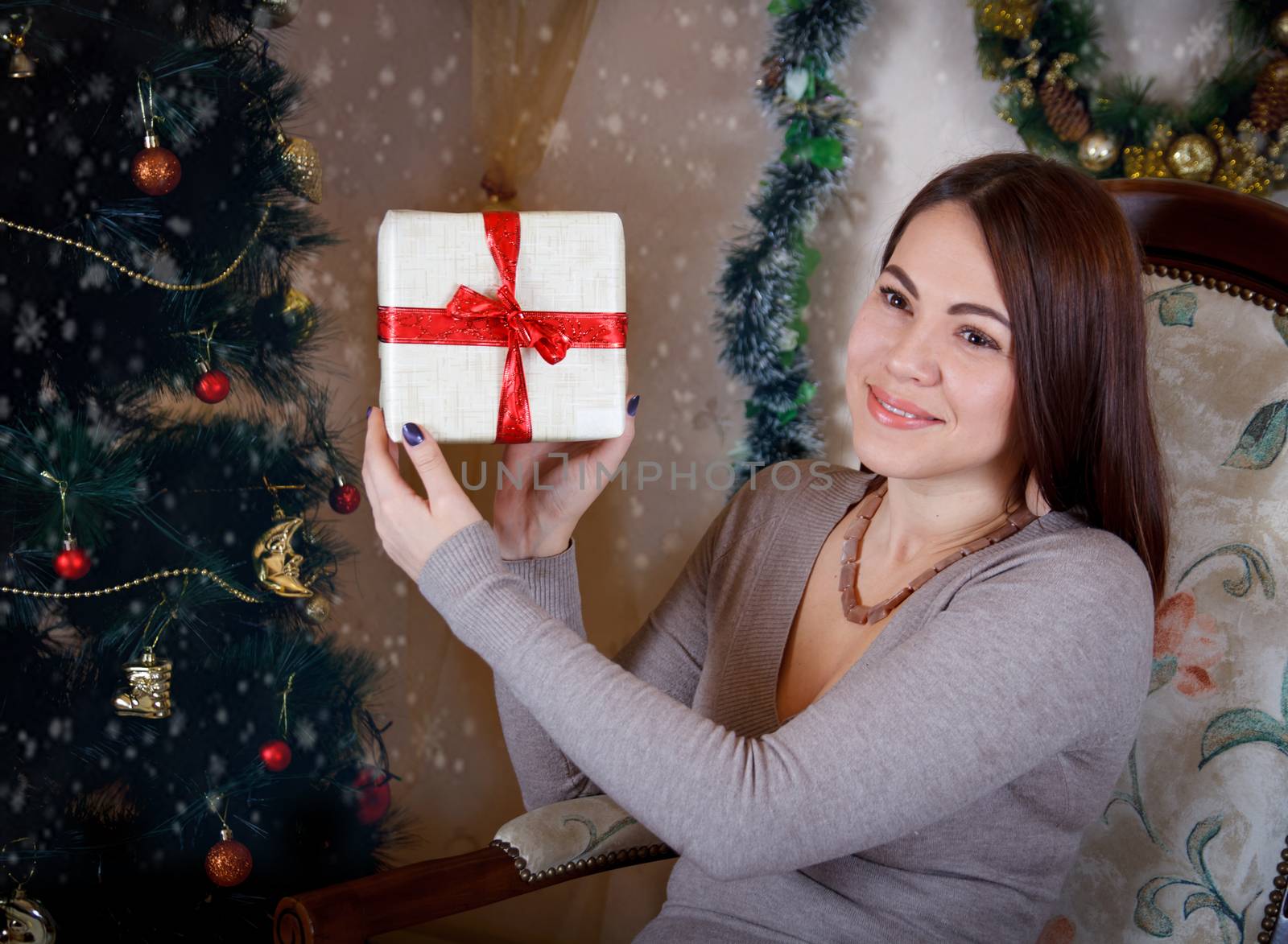 Pretty woman showing gift box under Christmas tree