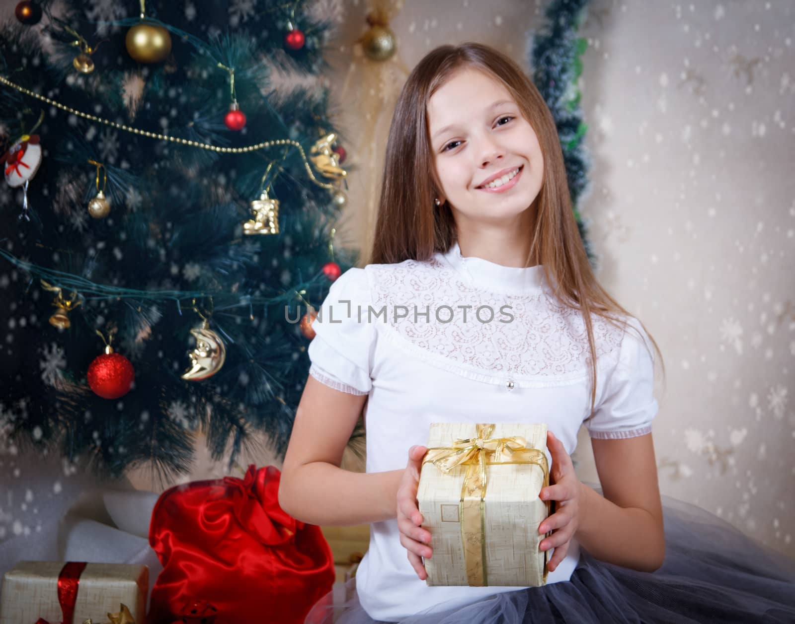 Smiling girl holding gift box under Christmas tree