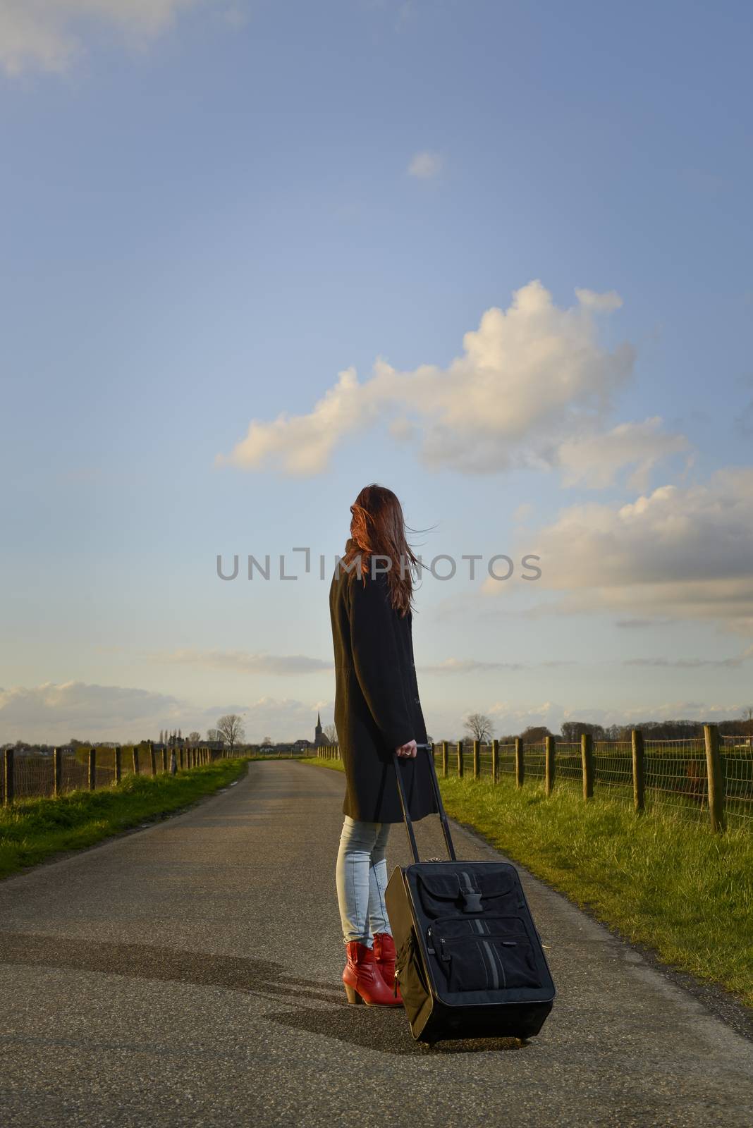 runaway girl standing with her suitcase on the road and look for the last time to her native village