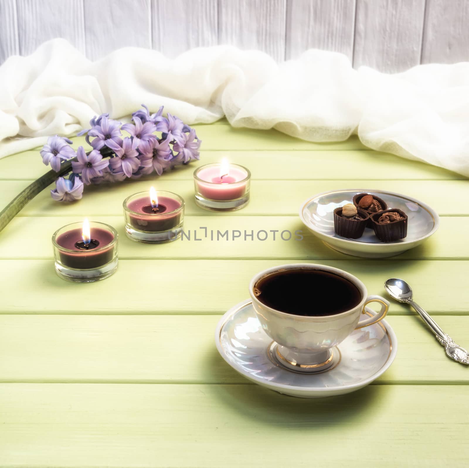 Cup of black coffee, candles and flowers on a wooden background.