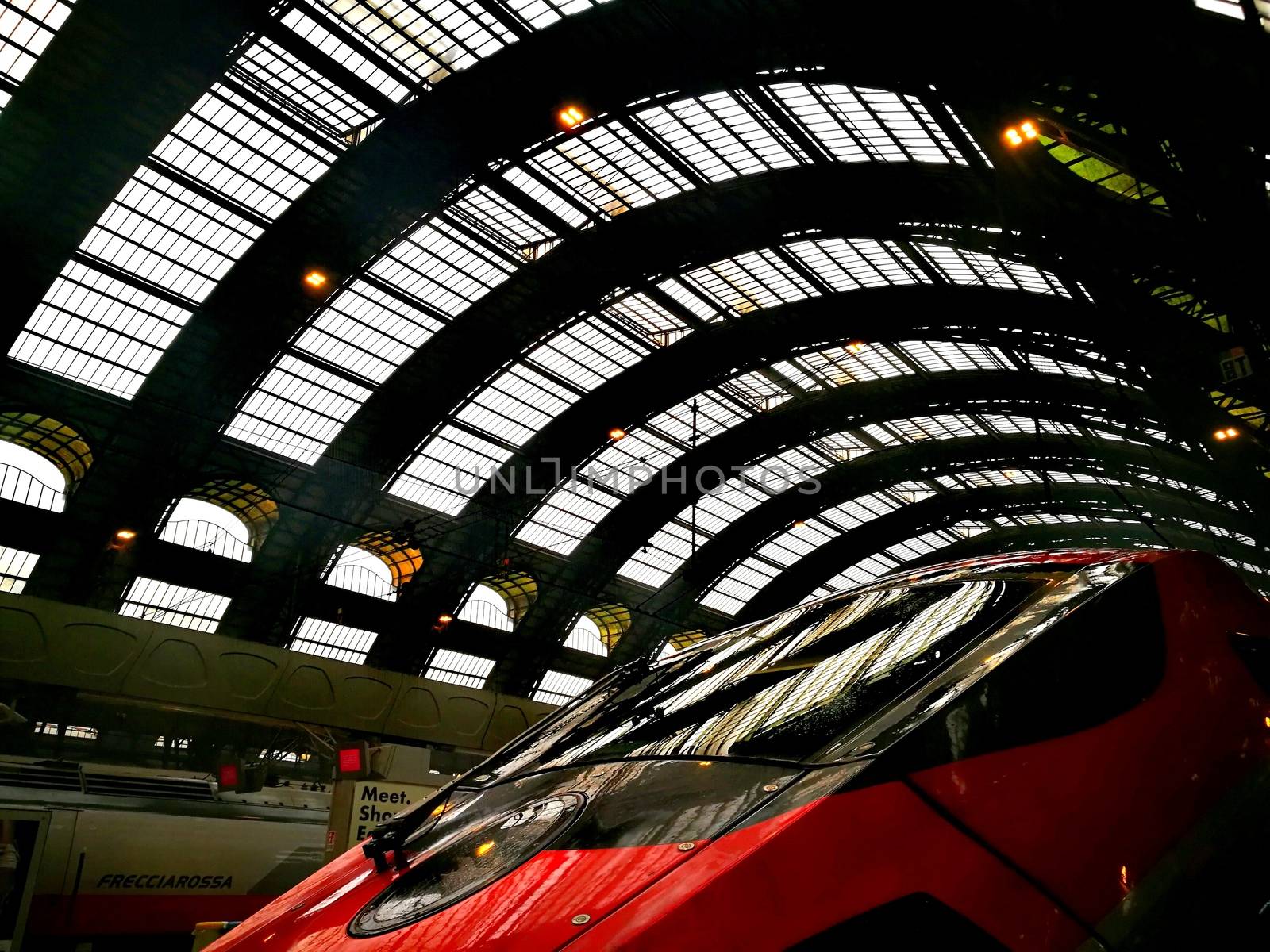 Architectural detail in Milan Central Station in Milan, Italy. Low angle view with dark shades and natural light from top. Red high velocity train close-up