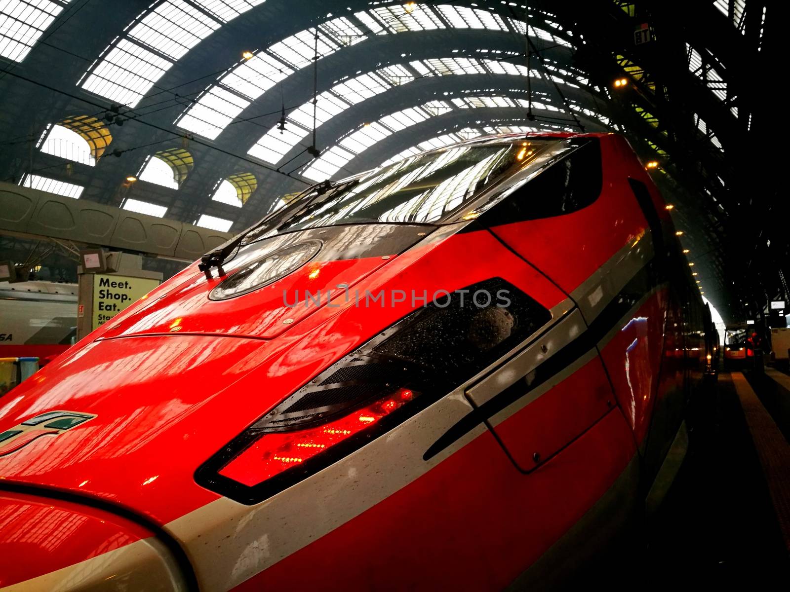 Architectural detail in Milan Central Station in Milan, Italy. Low angle view with dark shades and natural light from top. Red high velocity train close-up