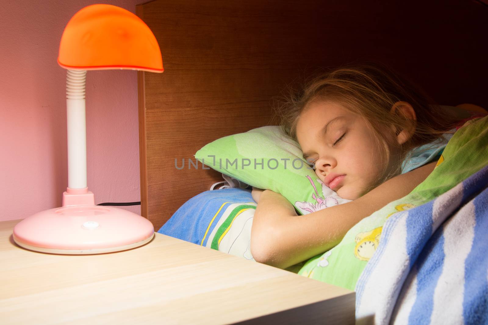 Seven-year girl asleep in bed, reading lamp is included on the next table