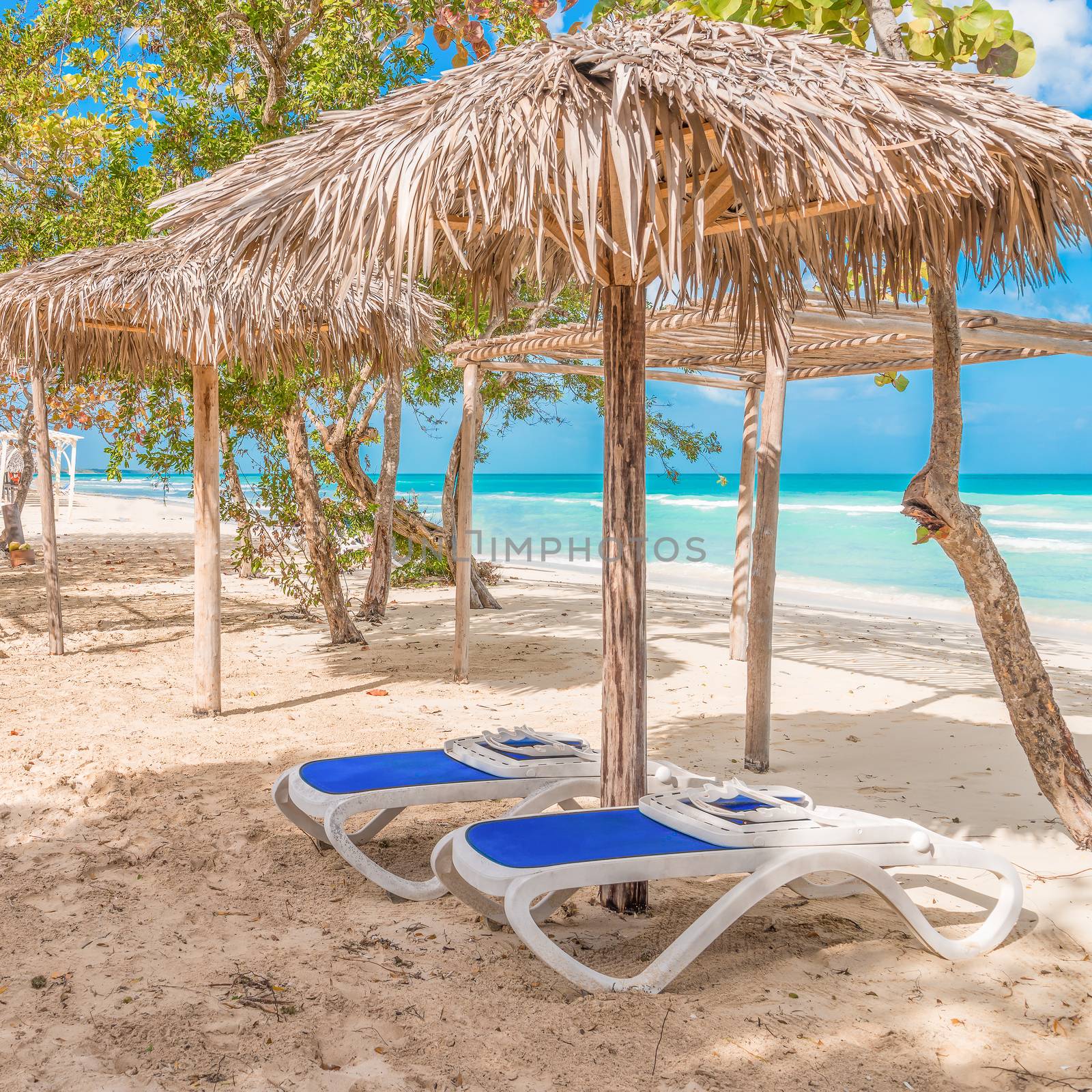 Two chairs await under a cabana at a quiet beach on the caribbean.