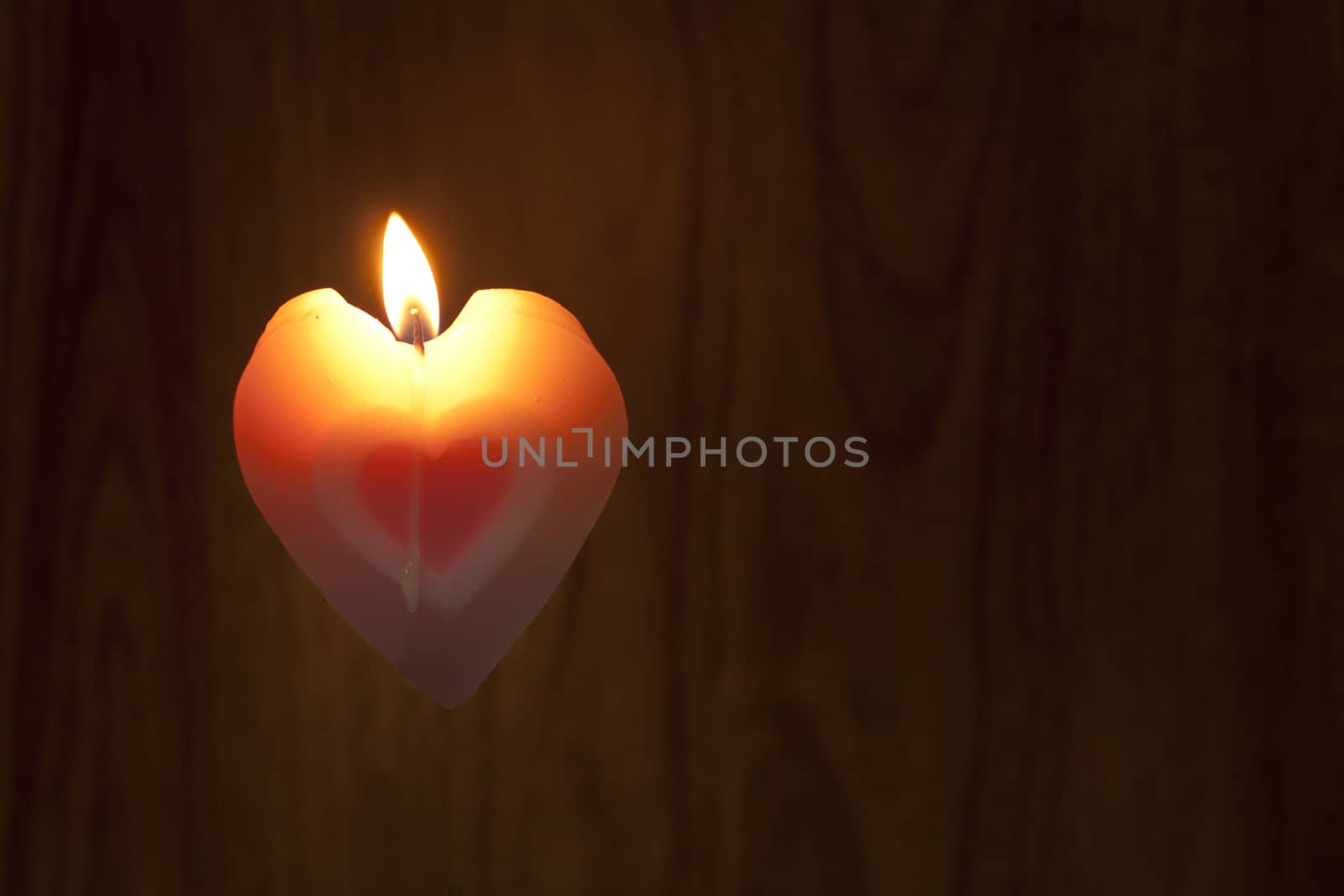 Candles shape heart pink color were lit on wood background. Love symbol for Valentine's day concept.