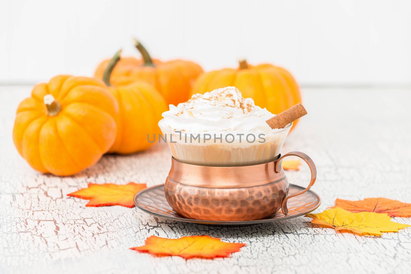Pumpkin spice latte surrounded by pumpkins and autumn leaves.